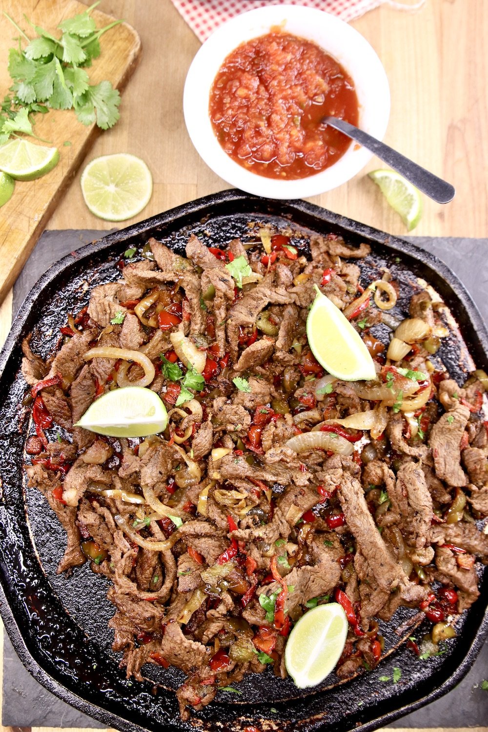 Griddle of steak fajitas with fresh limes. Bowl of salsa, cilantro