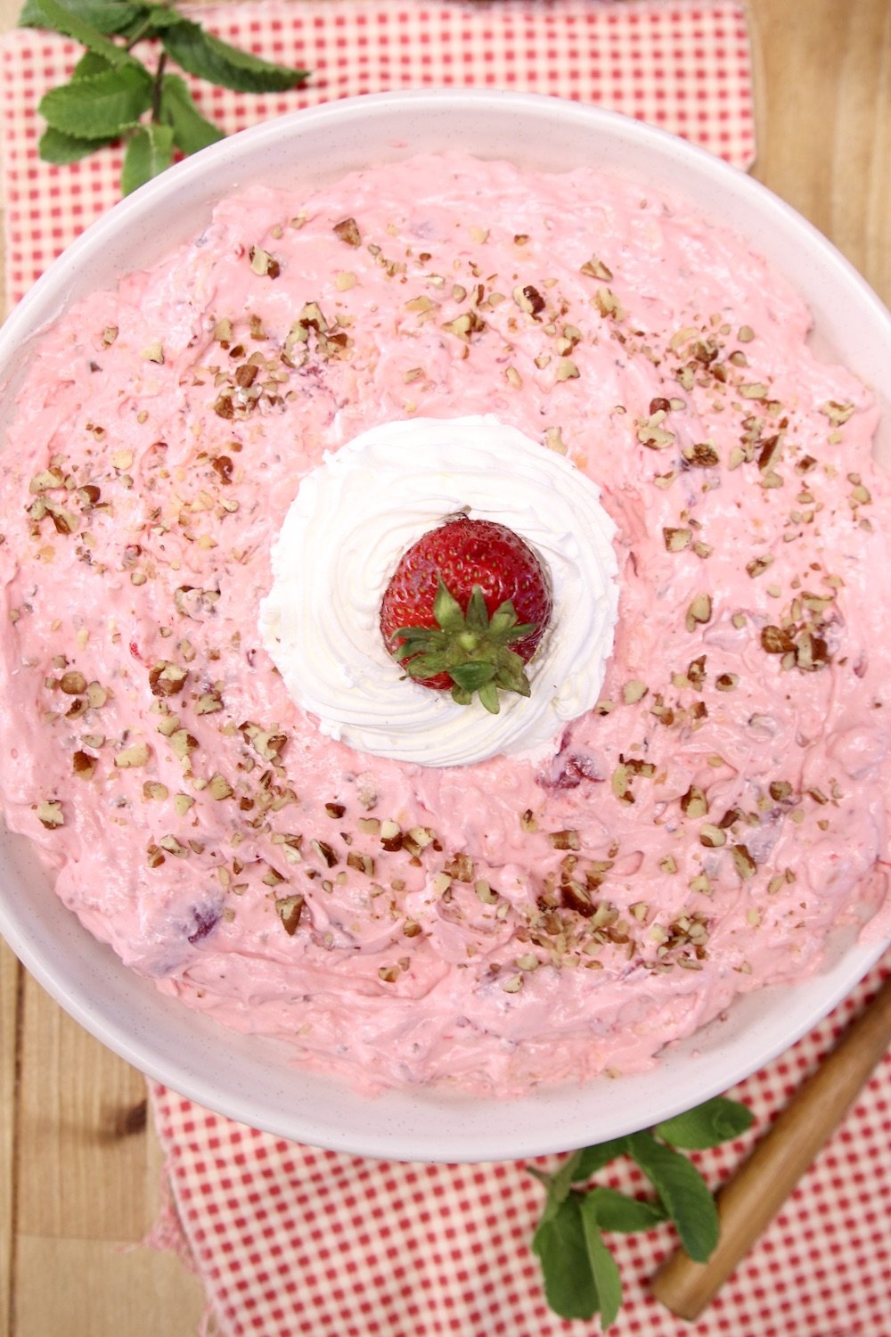 bowl of strawberry fluff with dollop of cool whip and a fresh strawberry, chopped pecans