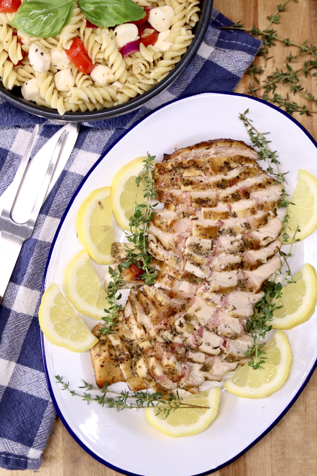 Chicken sliced on an oval platter, pasta salad in back ground