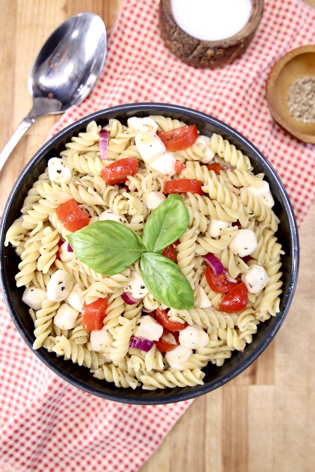 Pasta Salad with tomatoes, mozzarella, basil garnish in a black bowl
