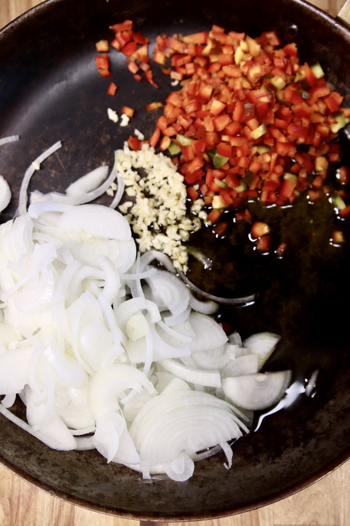 skillet with sliced onions, chopped bell peppers and minced garlic