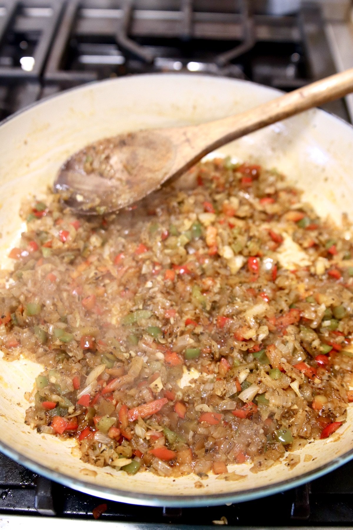 peppers and onions cooked in a large skillet with wood spoon