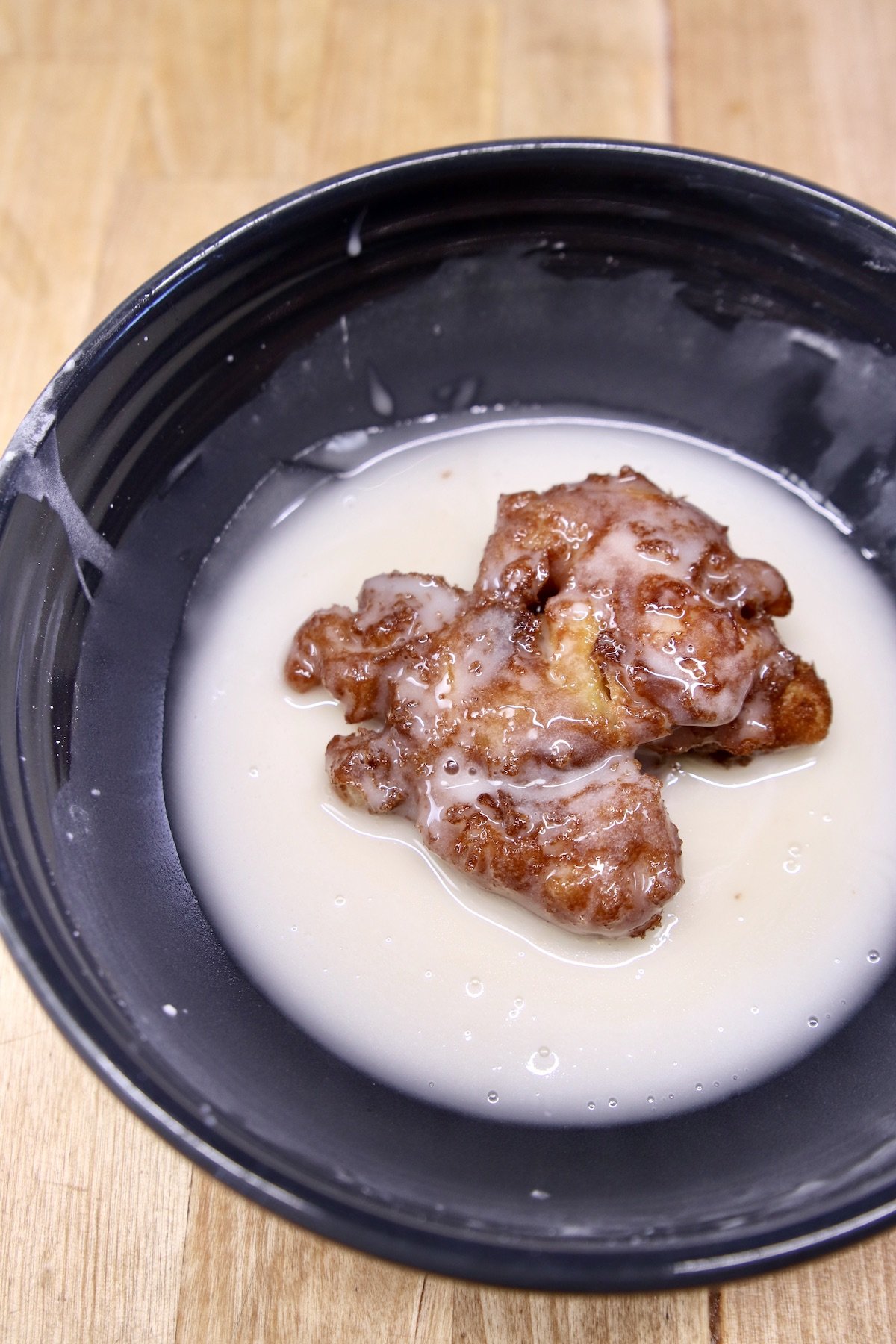 apple fritter dipping into powdered sugar glaze
