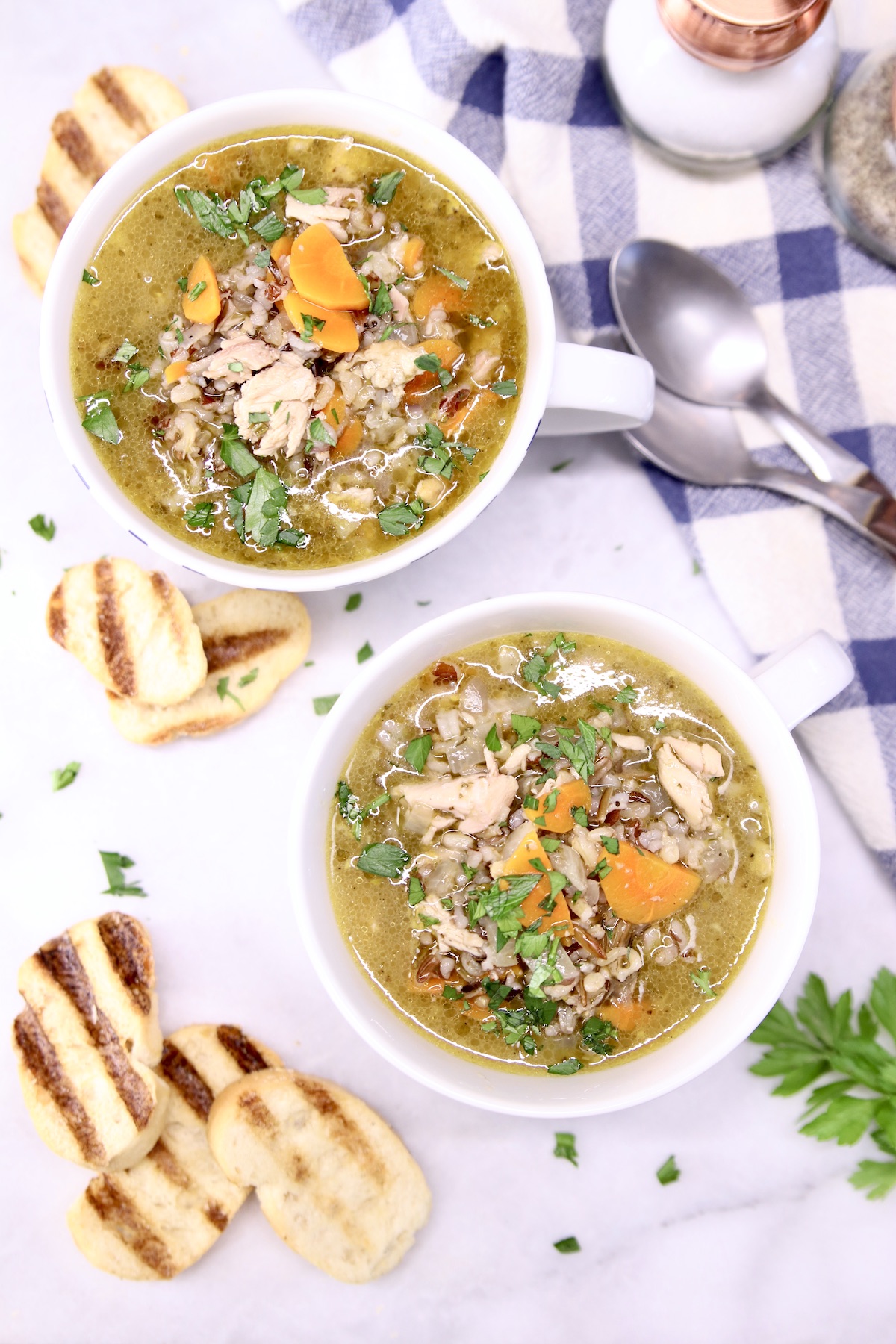 chicken and wild rice soup in 2 mugs, toasted baguette beside the mugs