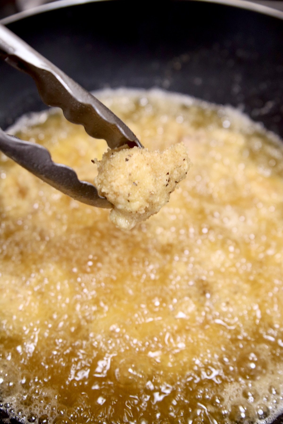 crispy fried breaded chicken in tongs over hot oil