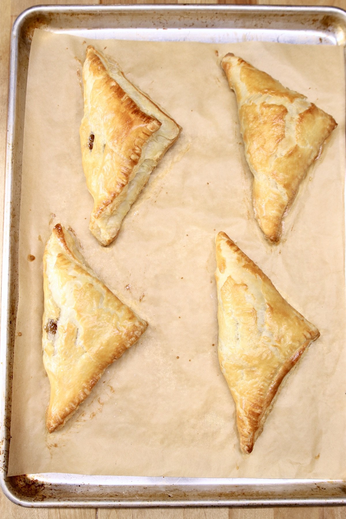 4 baked apple turnovers on a baking sheet with parchment paper