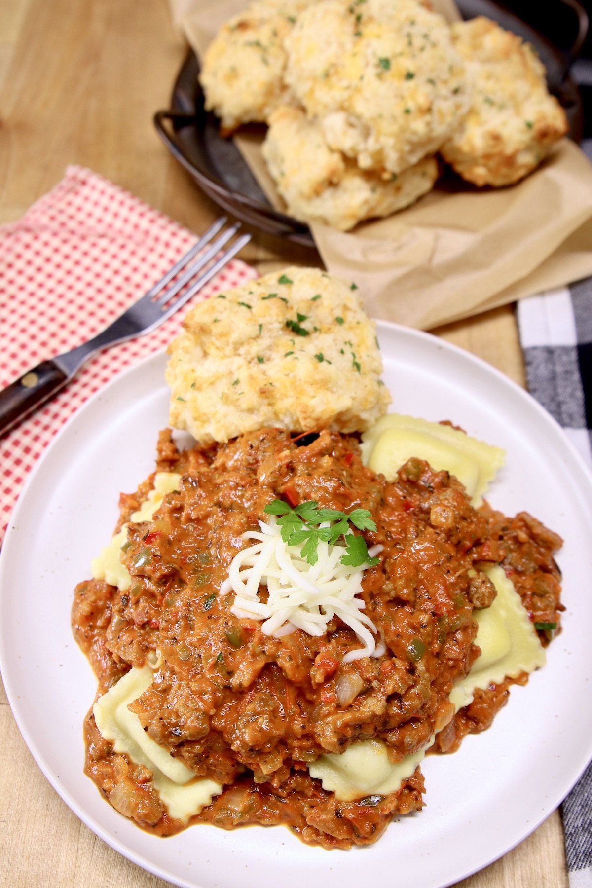 plate with ravioli and meat sauce with a biscuit, plate of biscuits in background