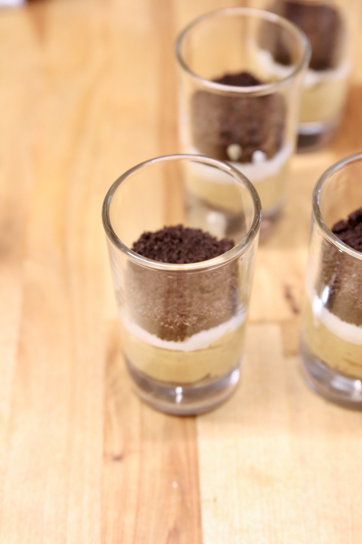 individual dessert glasses with layered no bake cheesecake, oreo crumbs