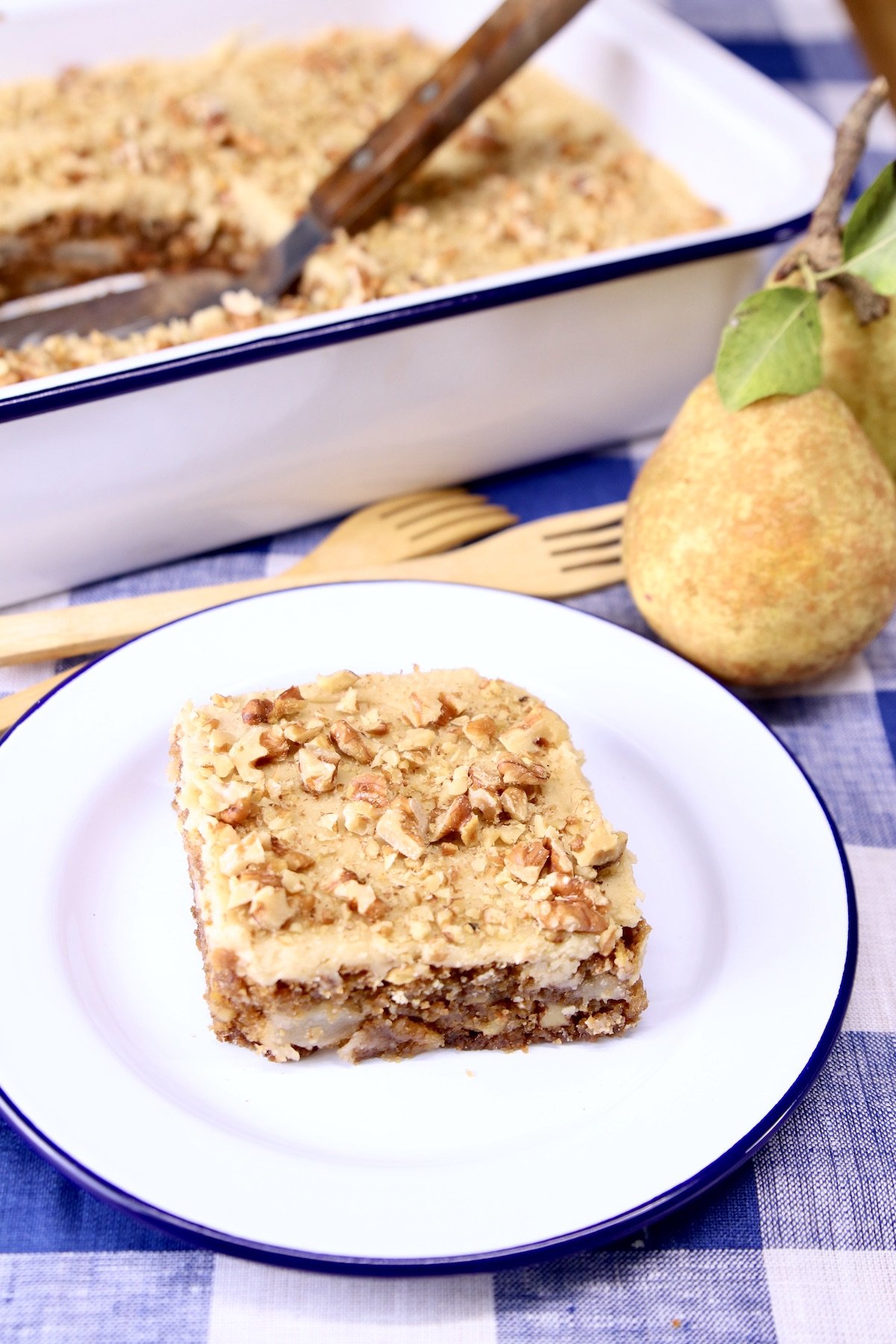 pear cake slice on a saucer, fresh pear and cake pan in background