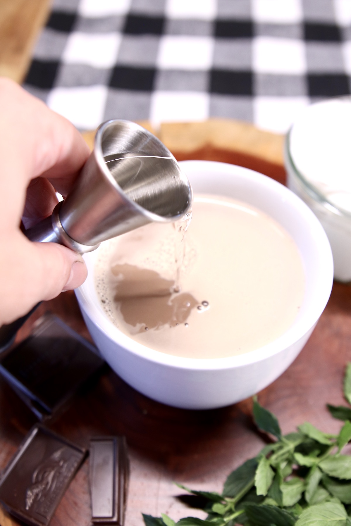 pouring peppermint schnapps into hot chocolate with a jigger