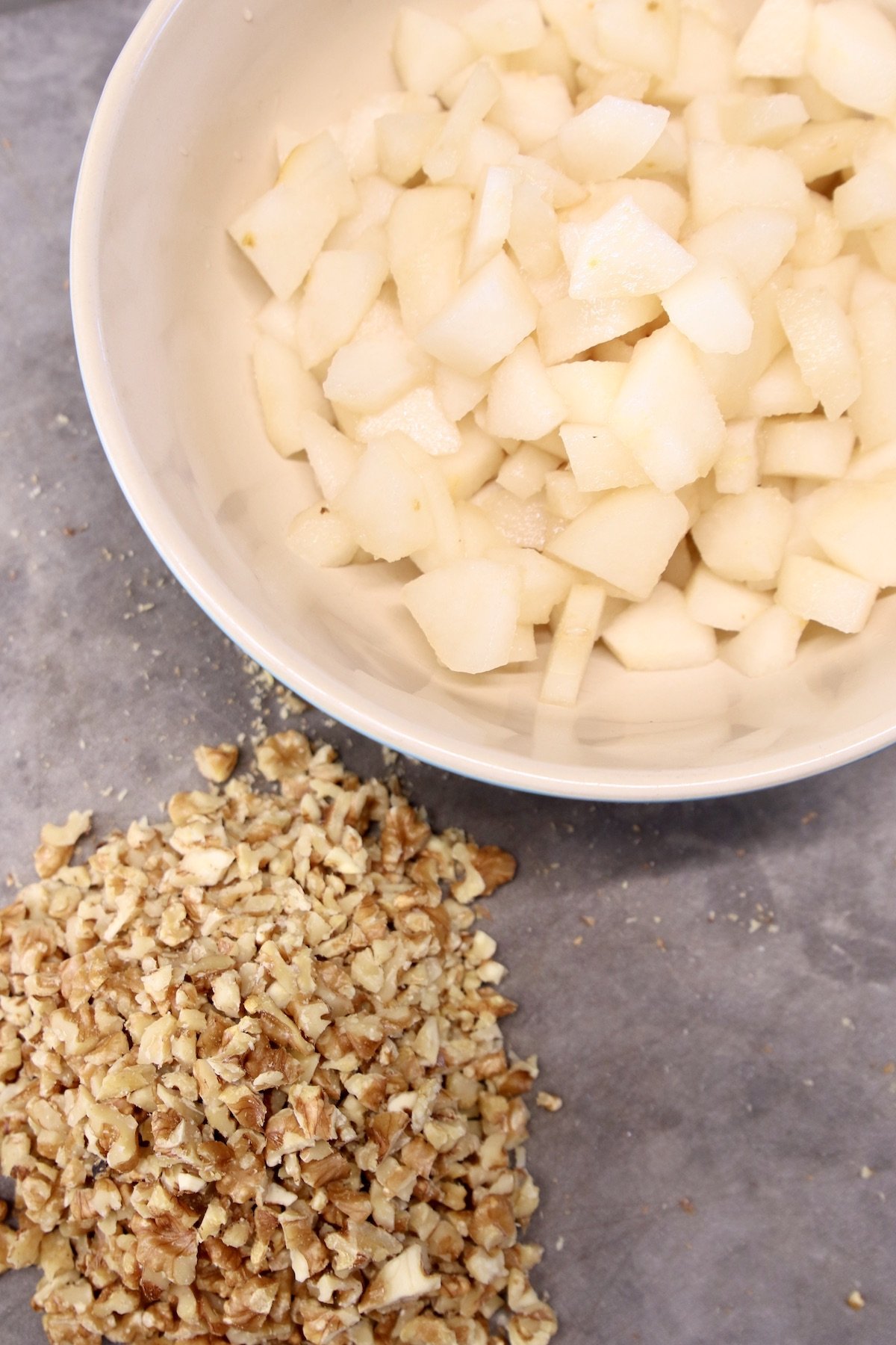 bowl of chopped pears, on a cutting board with chopped pecans