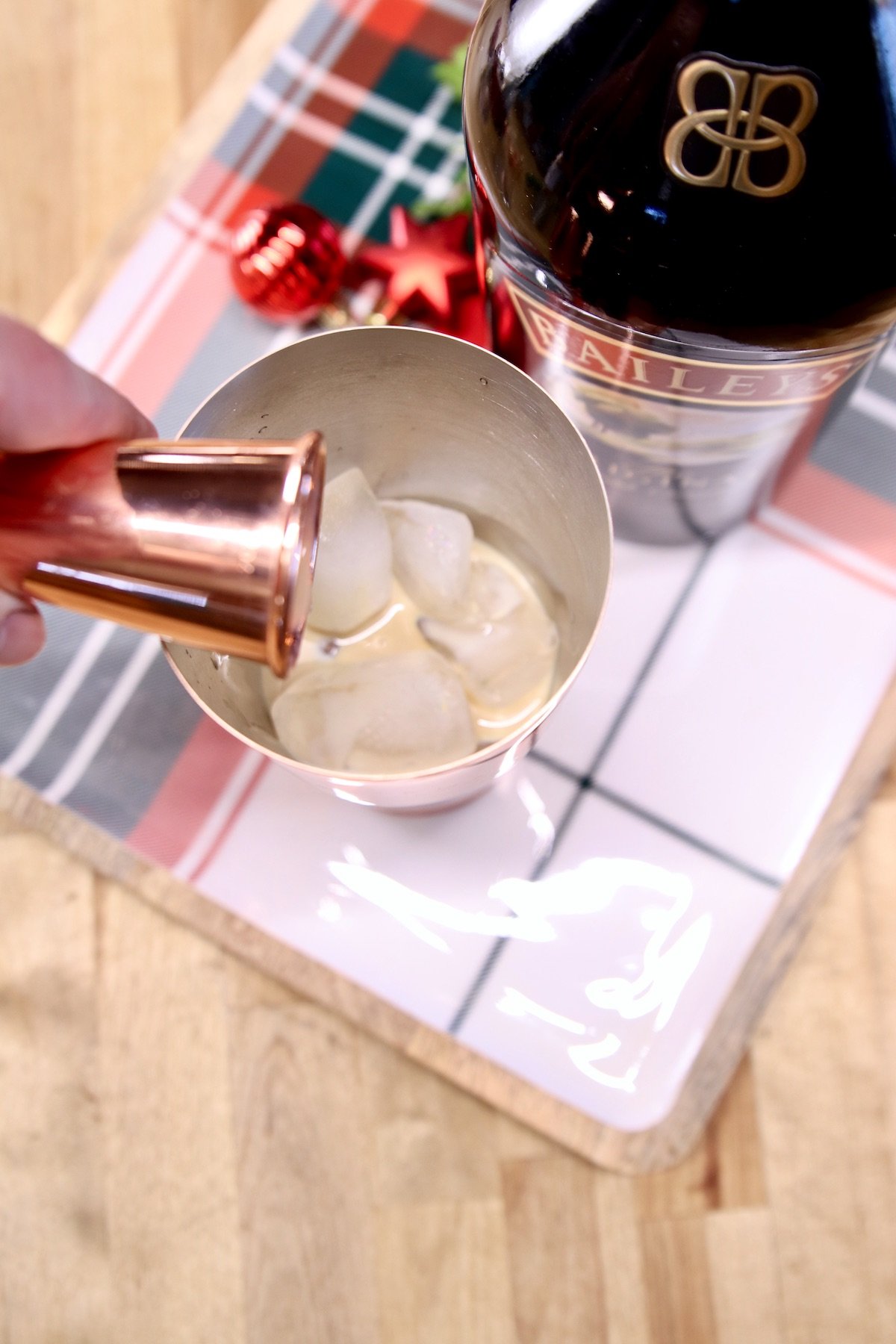 pouring bailieys irish cream into a cocktail shaker with ice