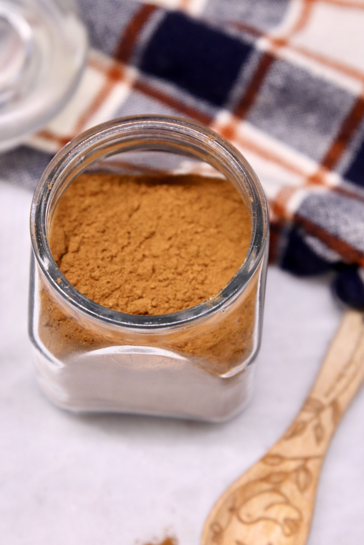 jar of pumpkin pie spice with plaid nampkin and small wooden spoon