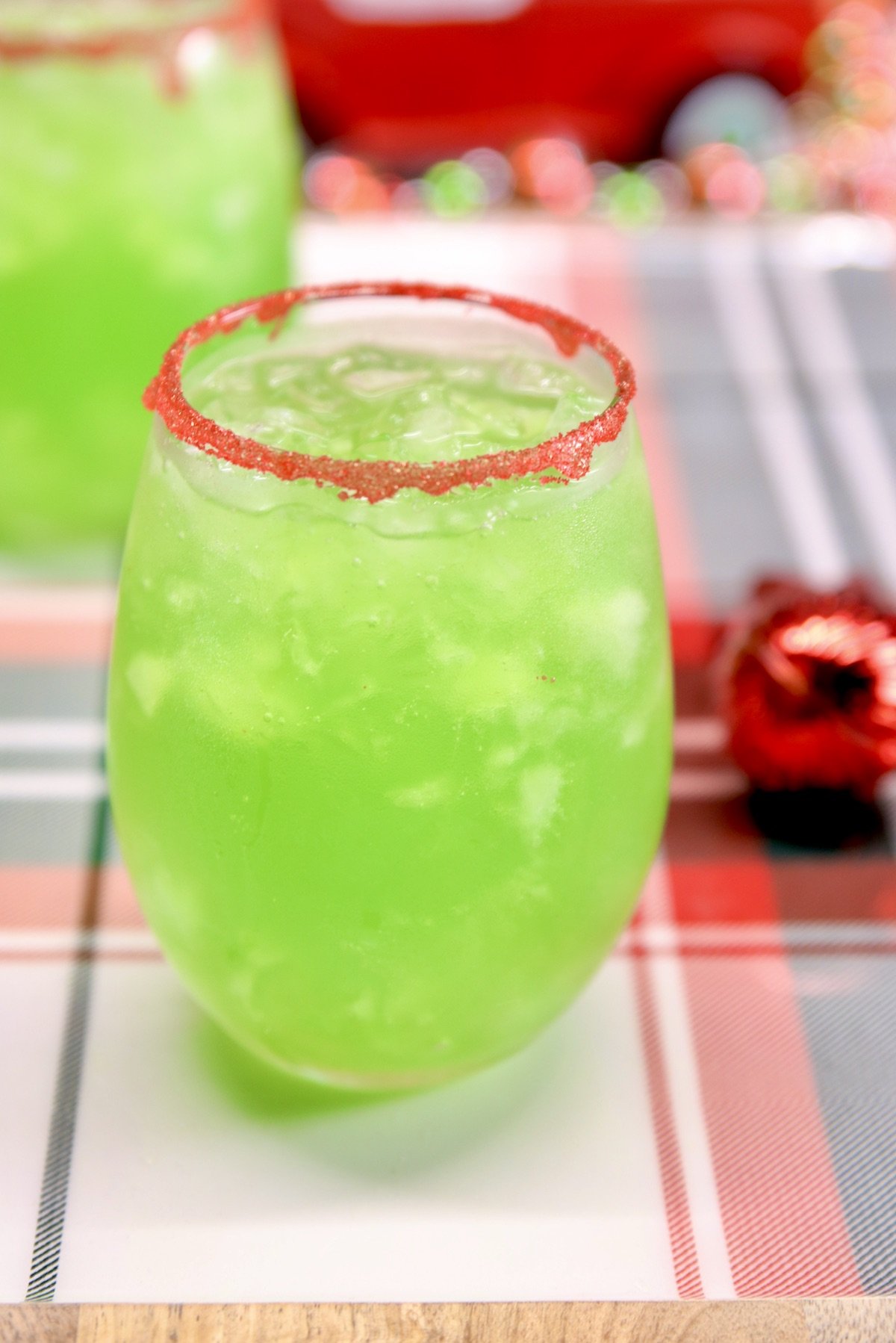 Grinch Punch is a fun party drink for Christmas made with vodka for the adults or without for the kids. A festive lemon-lime punch served up with a red sugared rim. lemon-lime green punch in 2 stemless wine glasses - red sugar rim