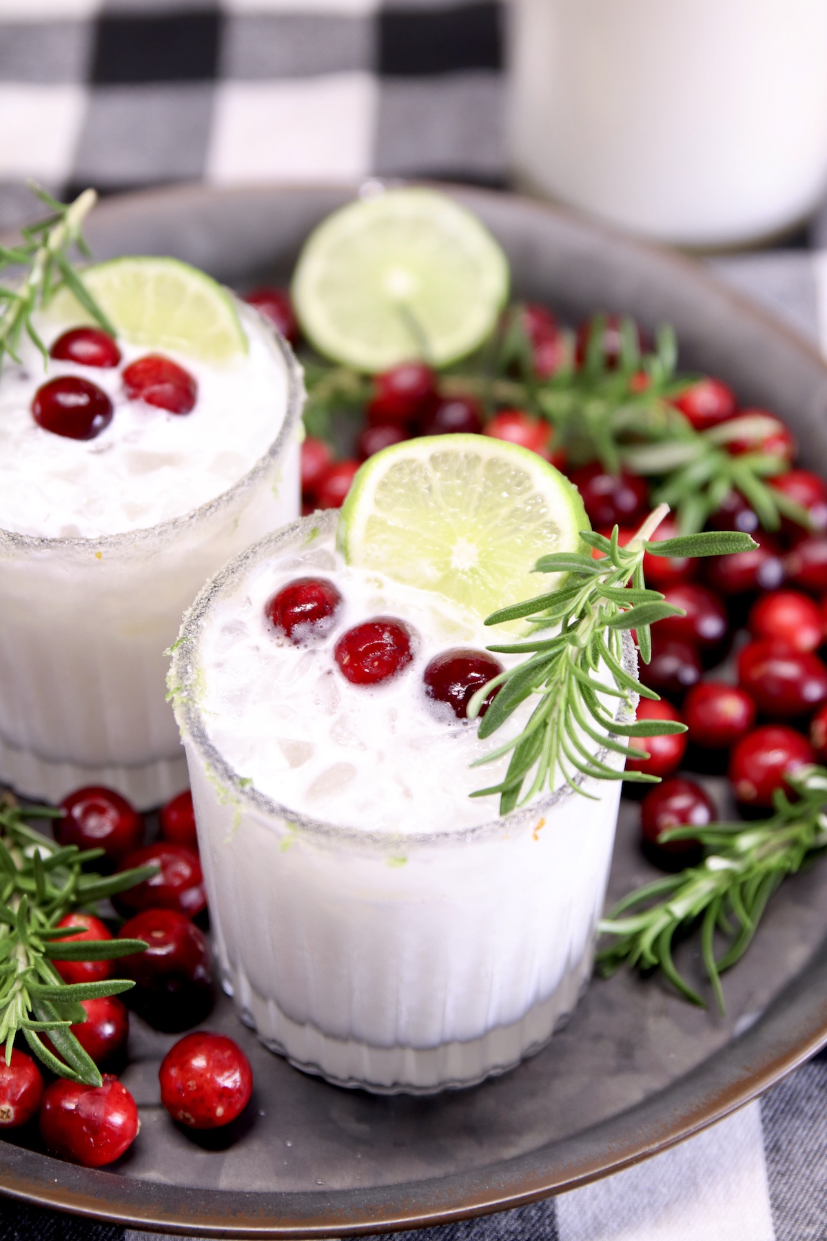 2 cocktail glasses of coconut margaritas on a tray - cranberry, rosemary and lime garnish