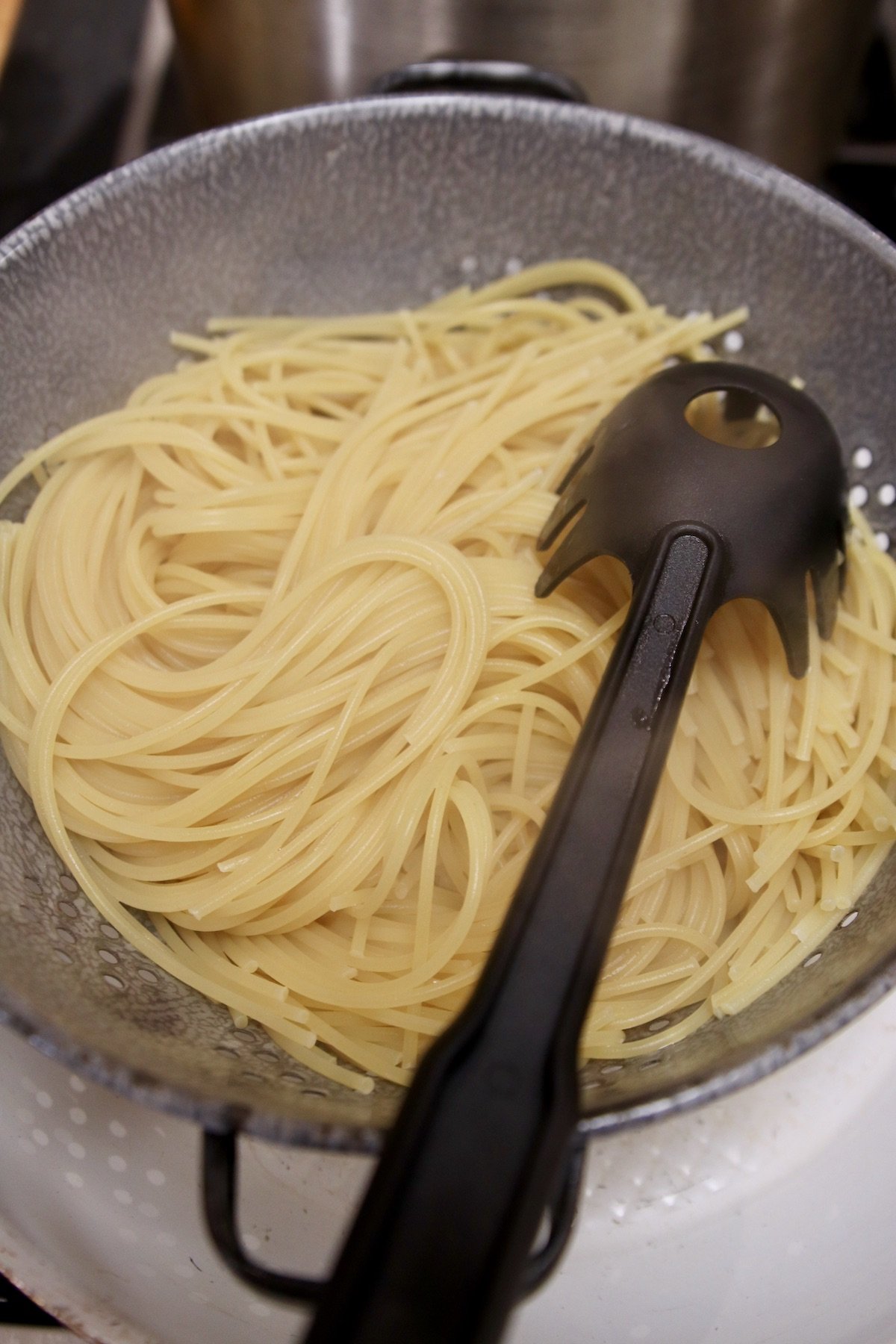 spaghetti draining in a colander with spaghetti spoon