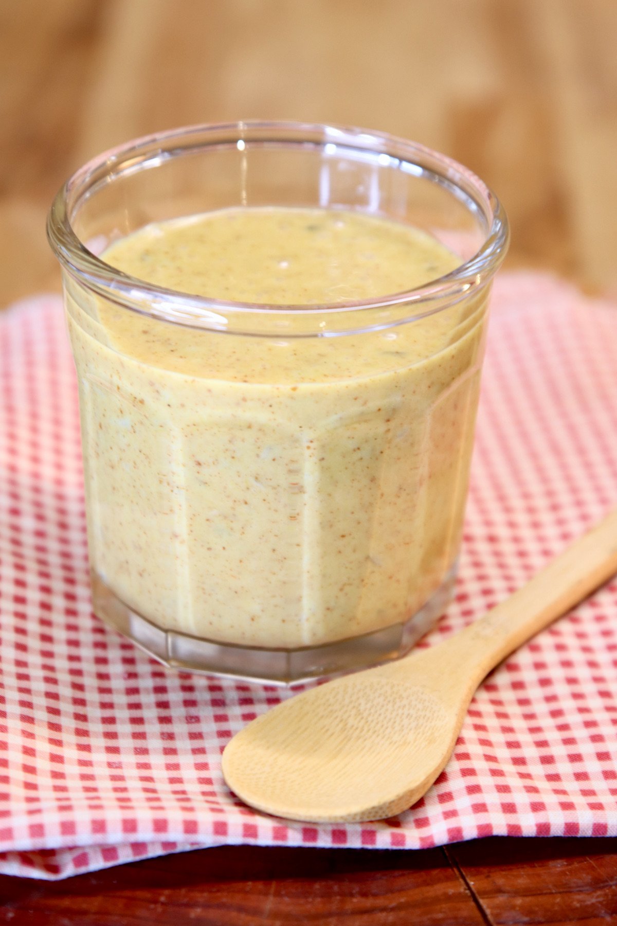 jar of jalapeno honey mustard with a bamboo spoon to the side on a red check napkin