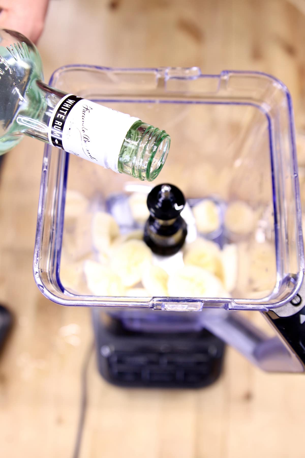 pouring rum into a blender with ice and bananas.