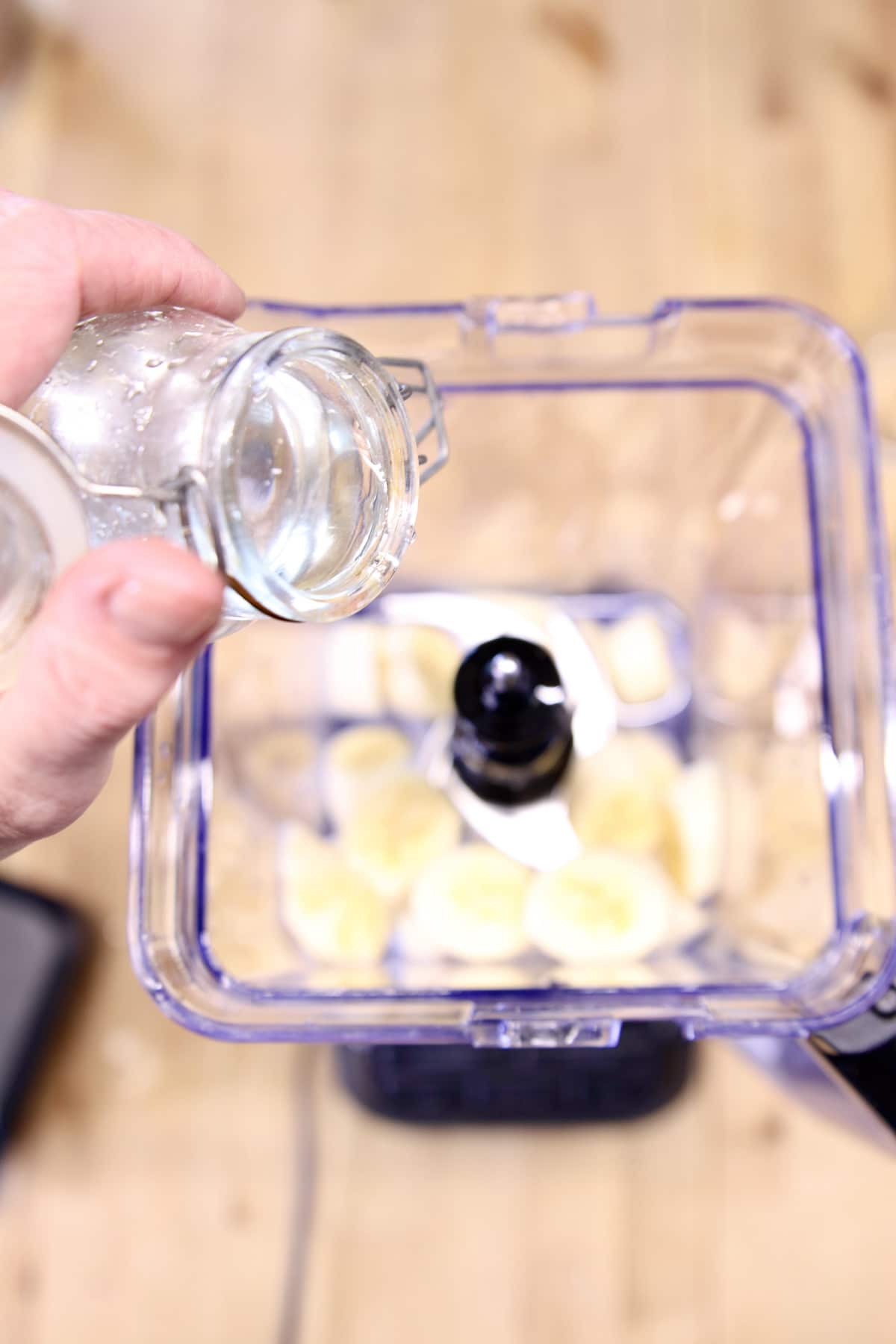 pouring simple syrup into a blender with bananas.