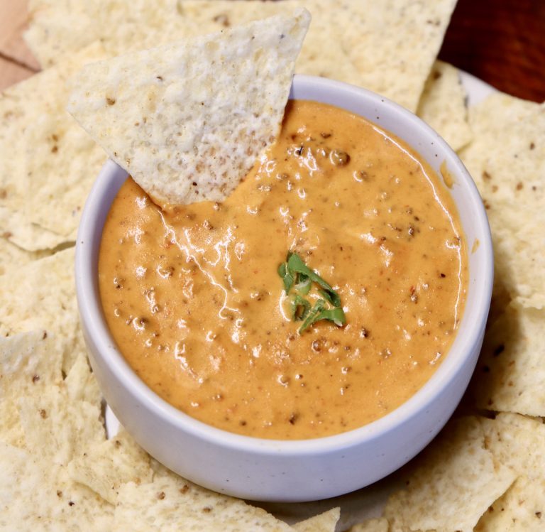 Chili Cheese Dip in a bowl with a tortilla chip dipping