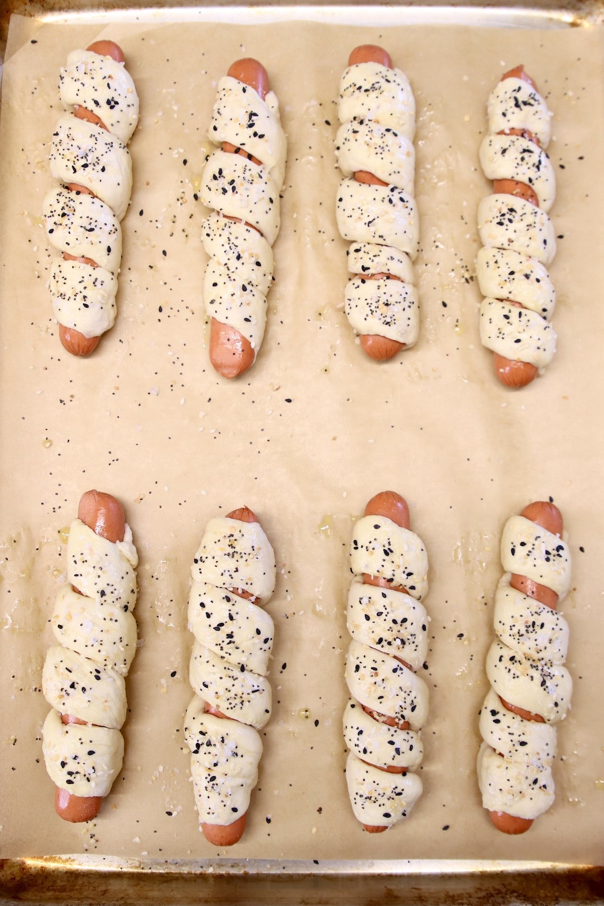 baking sheet with unbaked pretzel dogs topped with everything bagel seasoning.