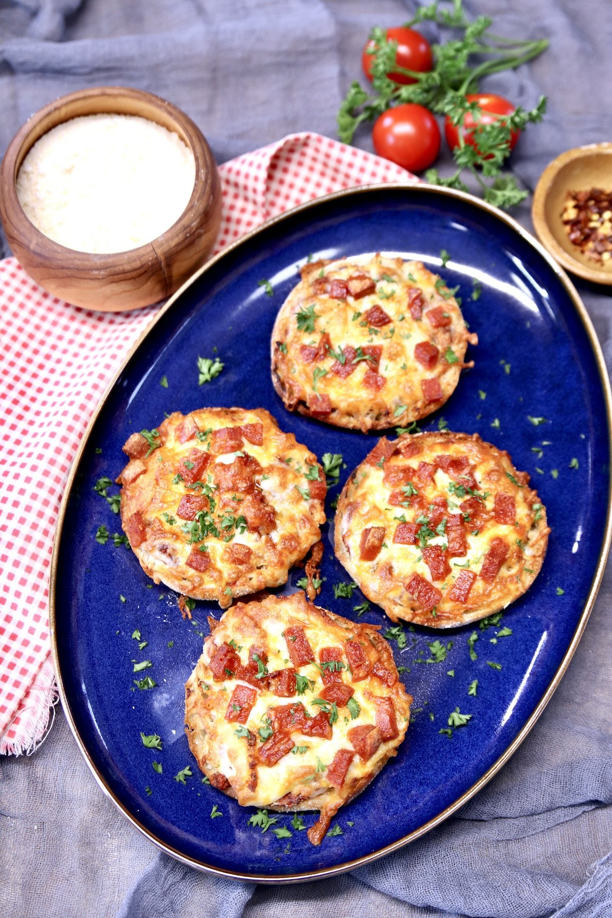 Platter of 4 mini pepperoni pizzas, bowl of parmesan cheese to the side.