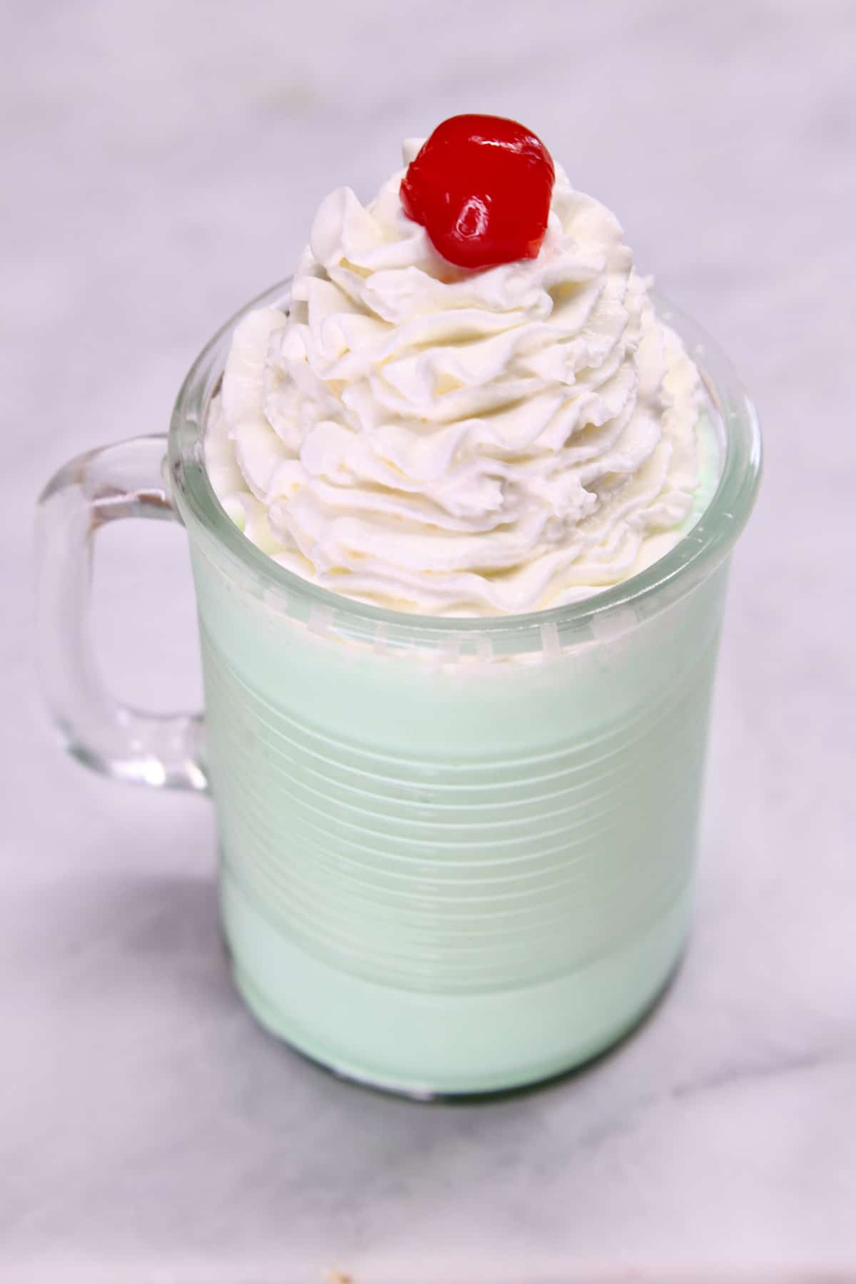Mug with mint shake topped with whipped cream and cherry.