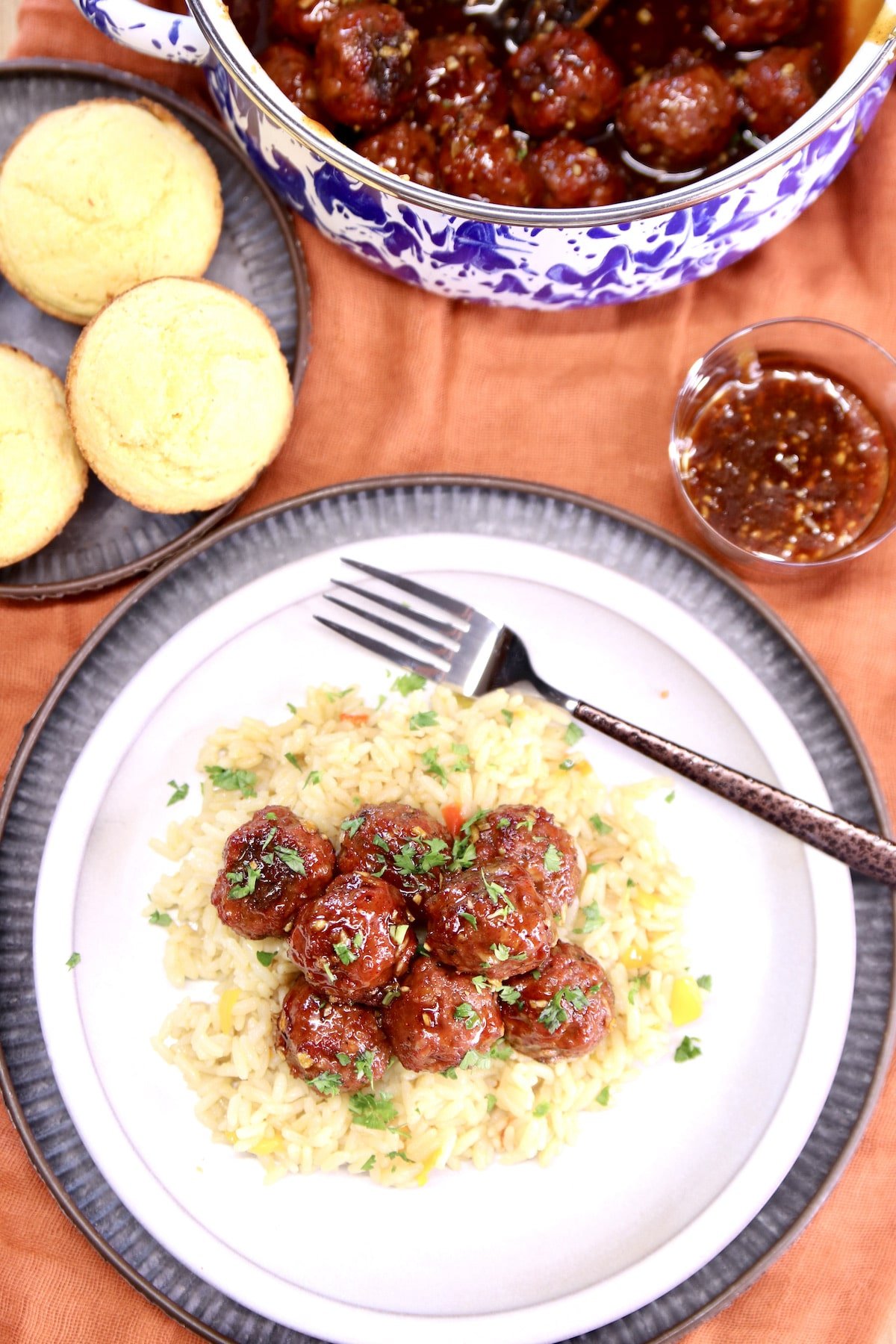 Meatballs over rice on a plate. Cornbread muffins and pan of meatballs in background.