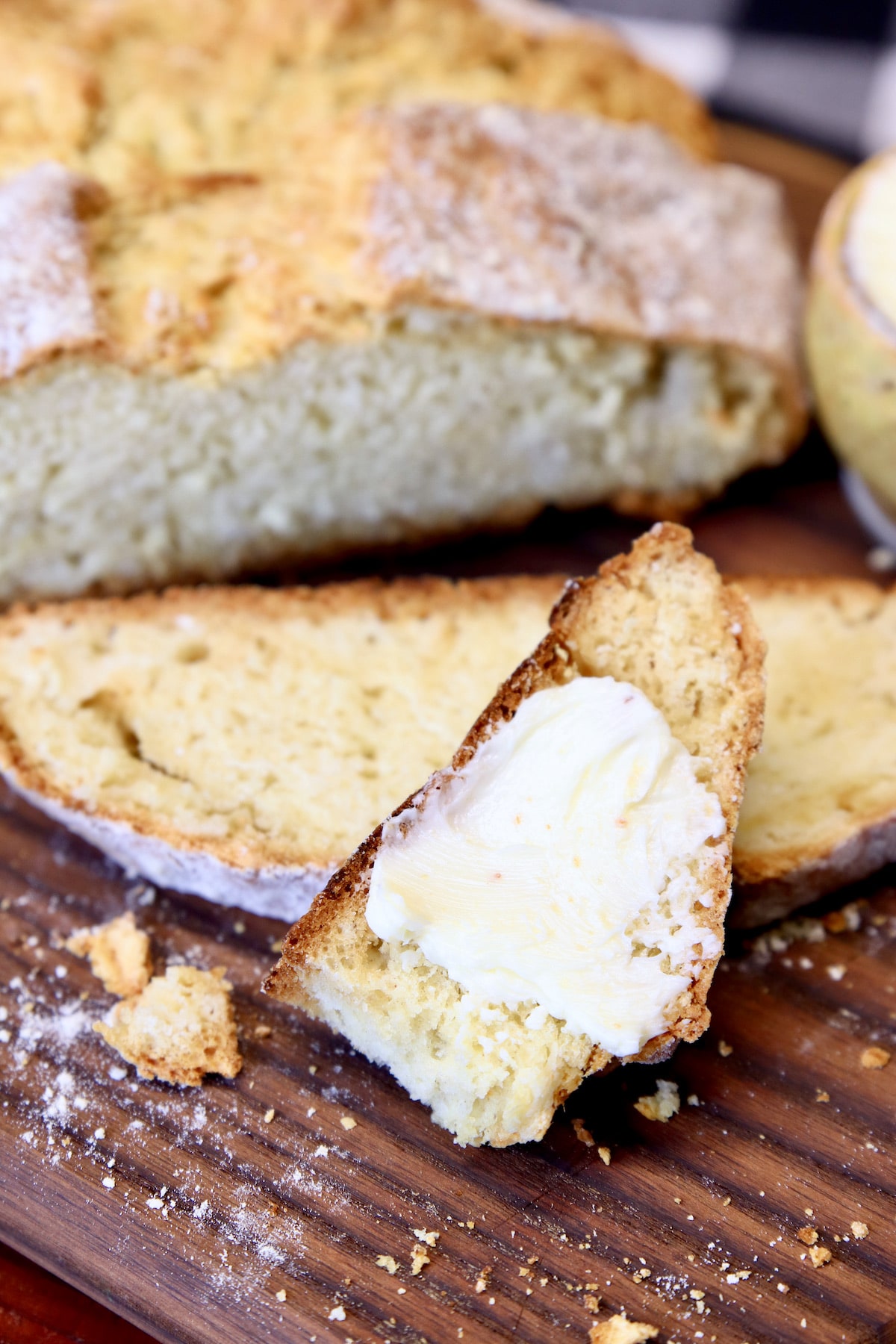 Closeup of slice of Irish Soda Bread with butter, with loaf.