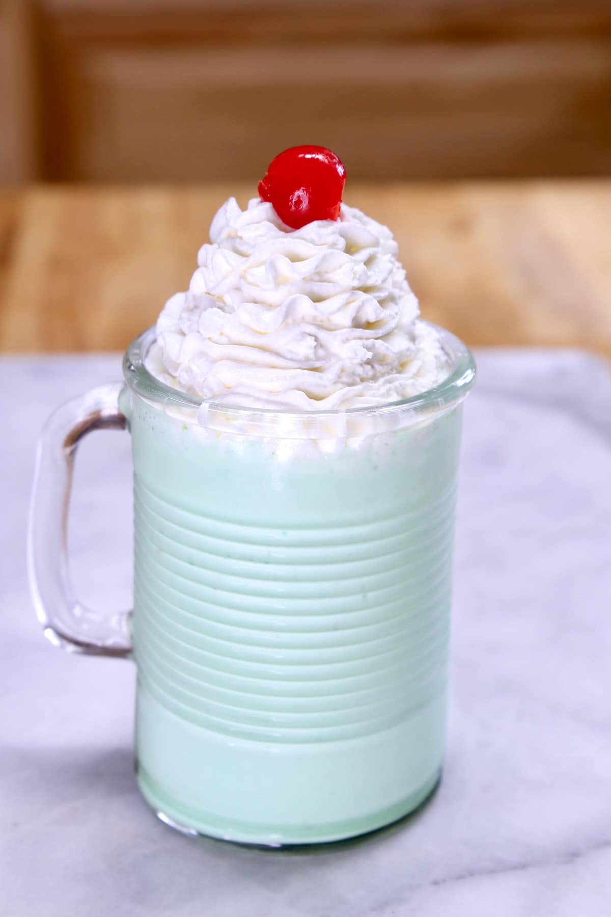 Mug with mint milkshake topped with whipped cream and a cherry on top.