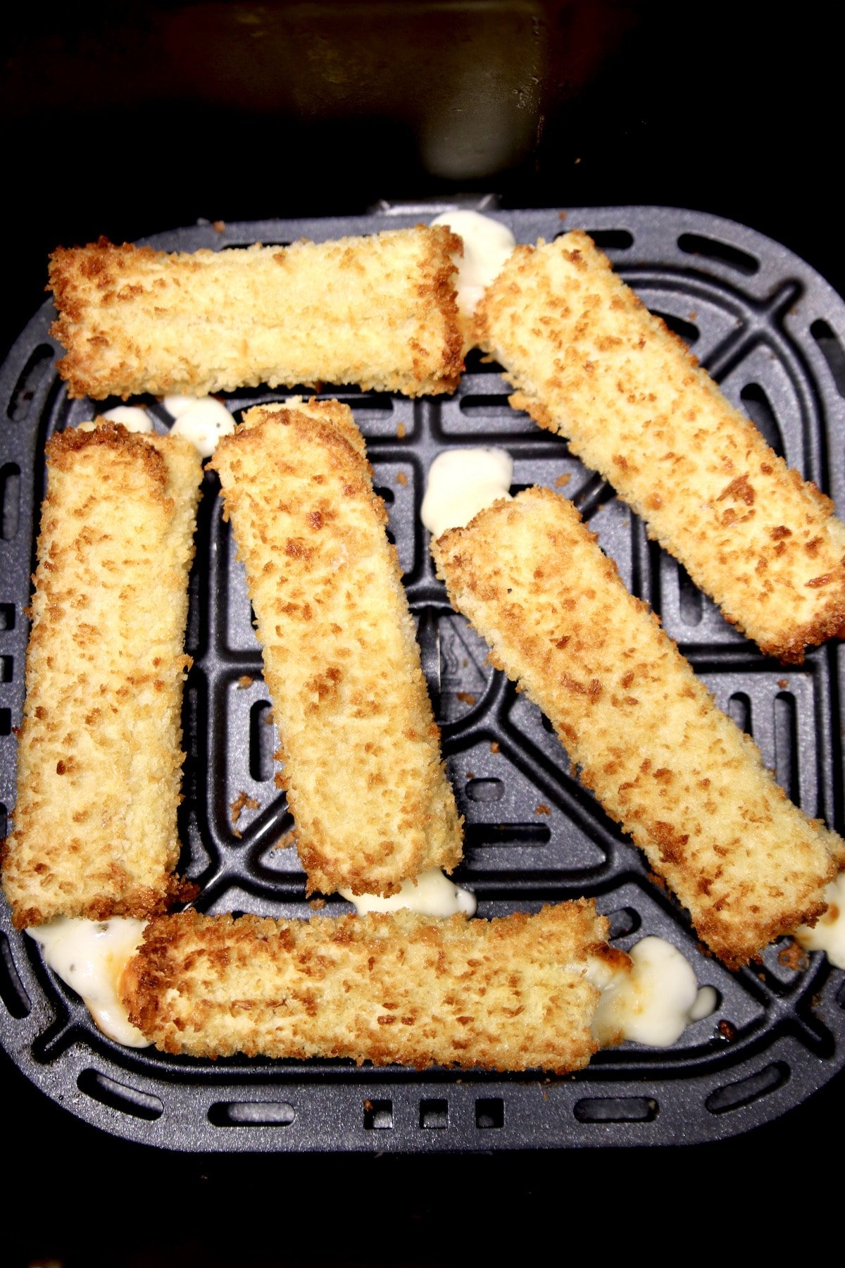 Crispy mozzarella sticks in air fryer basket.