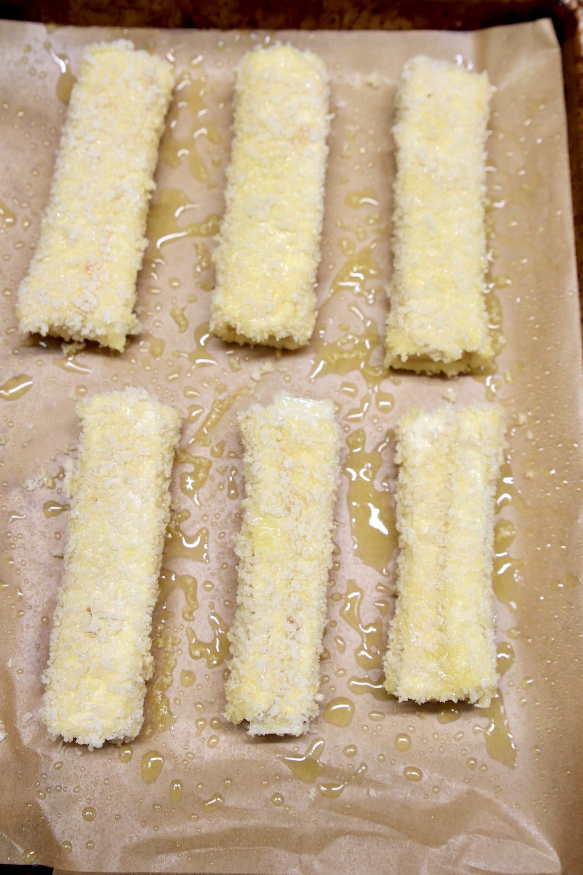 baking sheet with 6 cheese sticks coated in panko and olive oil.