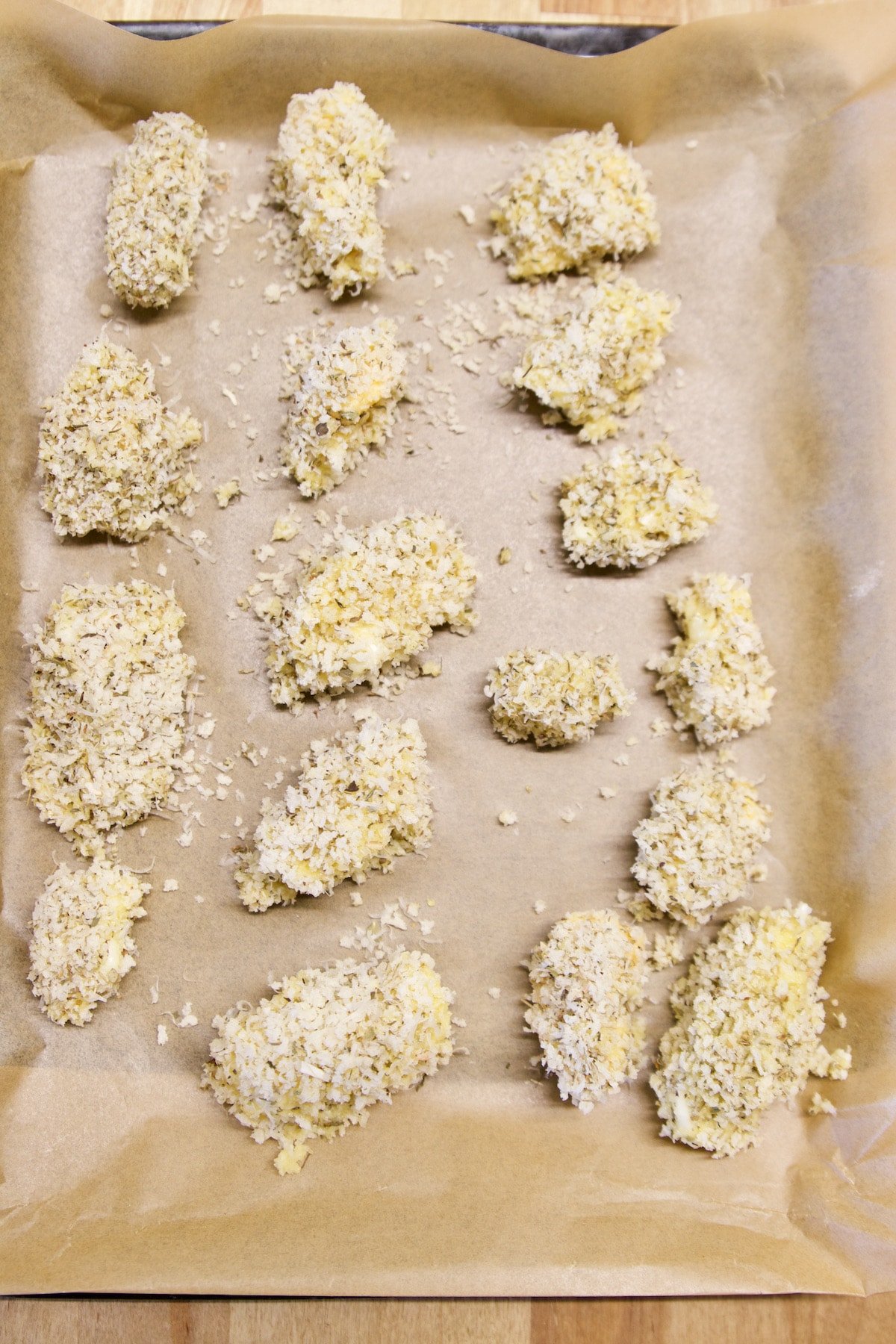 breaded cheese curds on a lined baking sheet.
