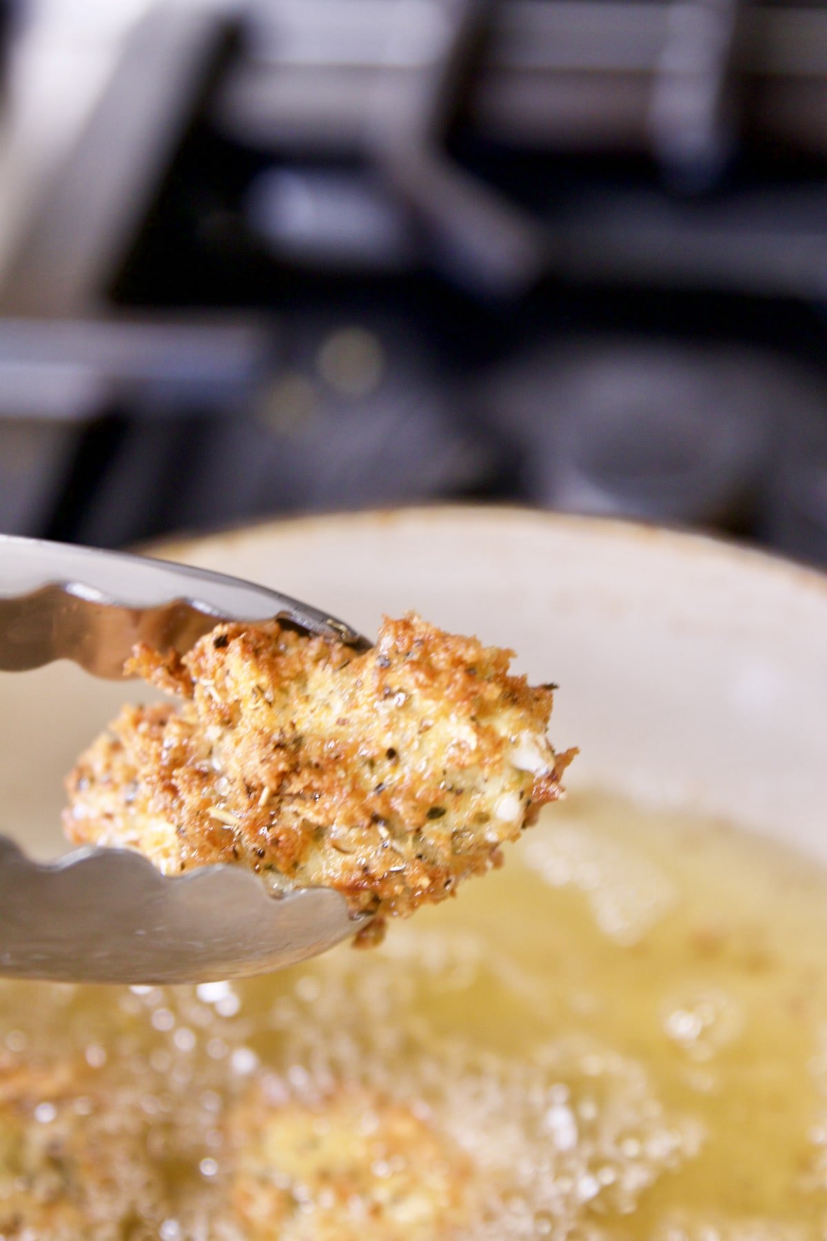 Fried cheese curd held with tongs.