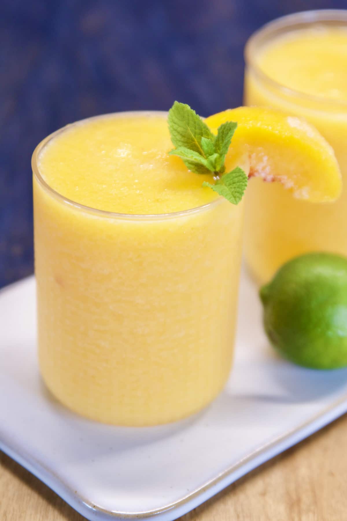 Peach daiquiri in a small glass, peach and mint garnish.