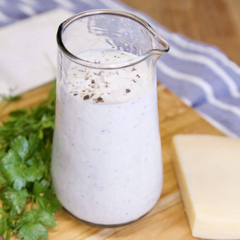 Ranch Dressing in a small glass pitcher. Fresh parsley and chunk of Parmesan cheese on cutting board.