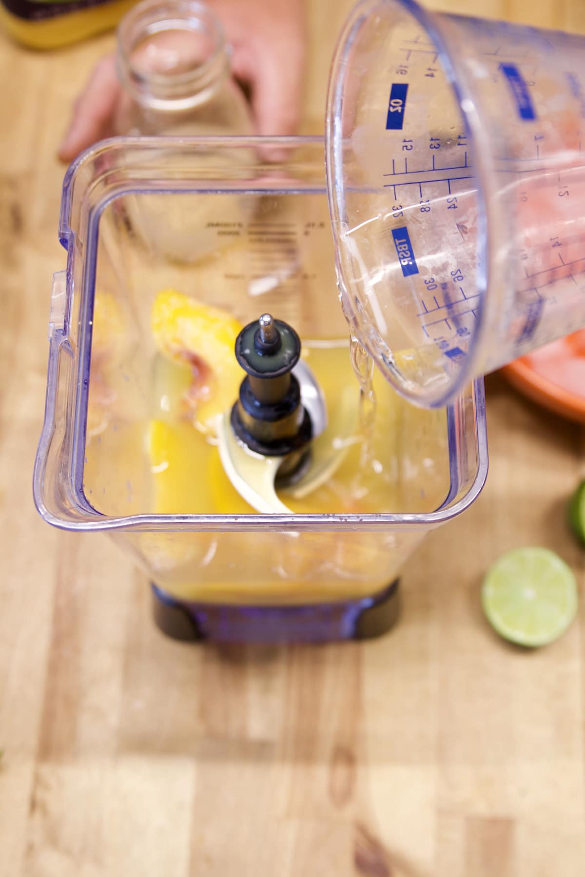 Pouring simple syrup into blender with peaches.