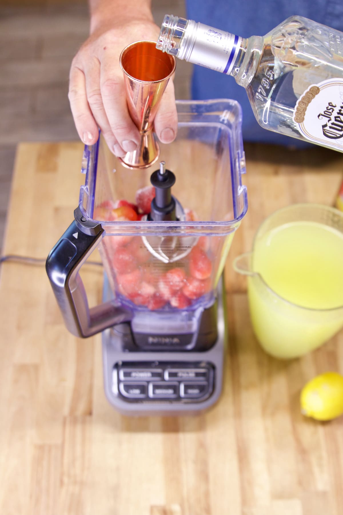 Pouring tequila into blender with strawberries.