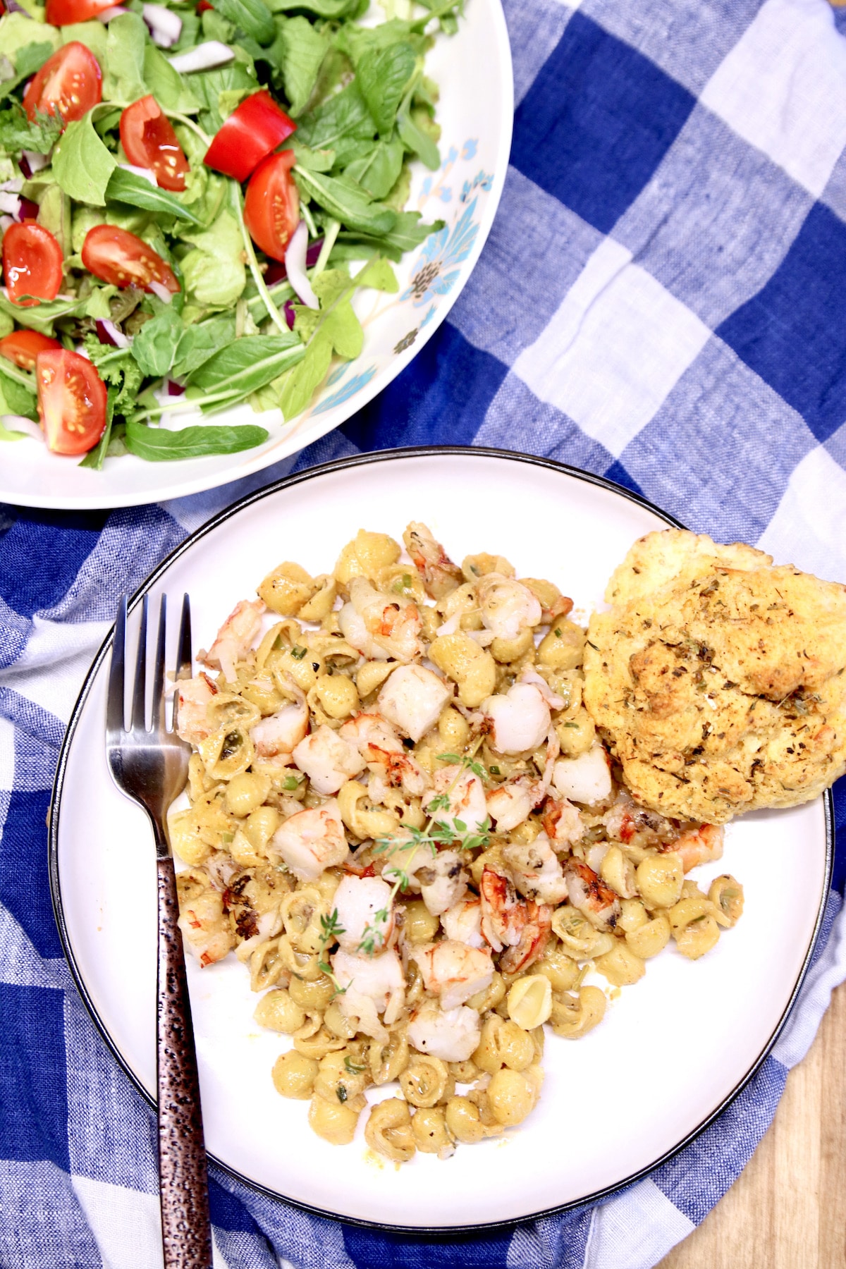 Plate of Cajun shrimp pasta with a biscuit. Plate of salad.