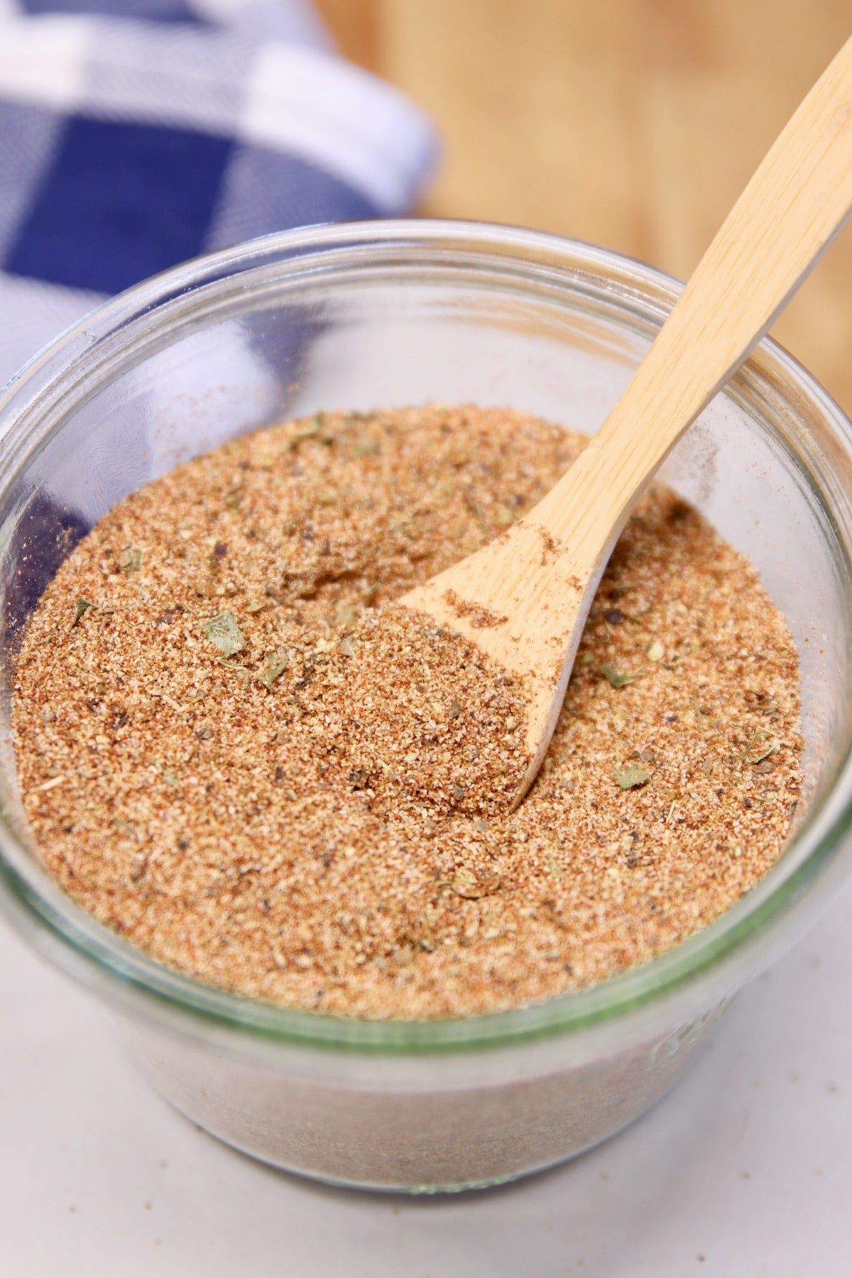 Jar of Creole seasoning with small wood spoon.