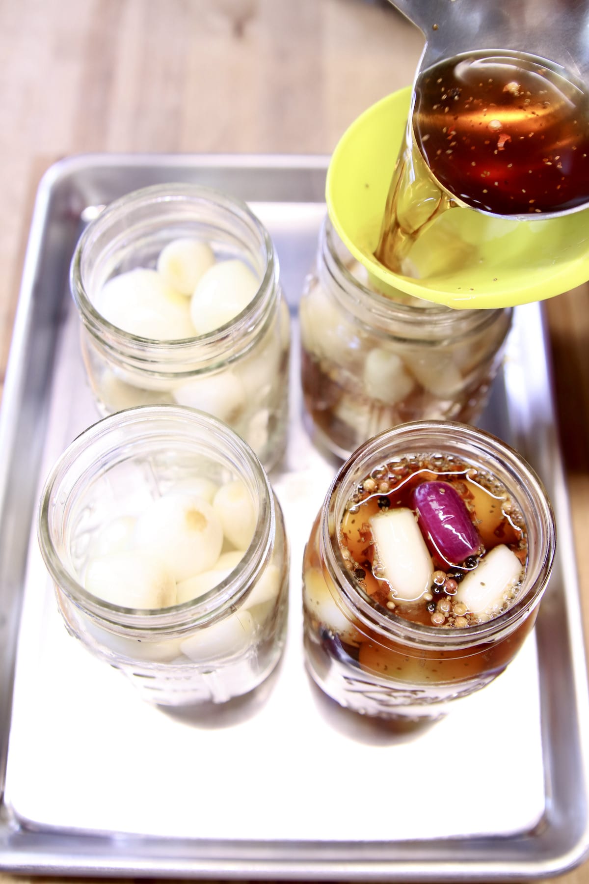 Pouring malt vinegar brine over onions in jars.