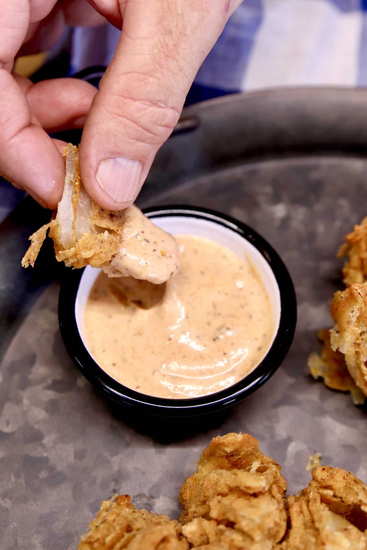 Dipping blooming onion petal into sauce.