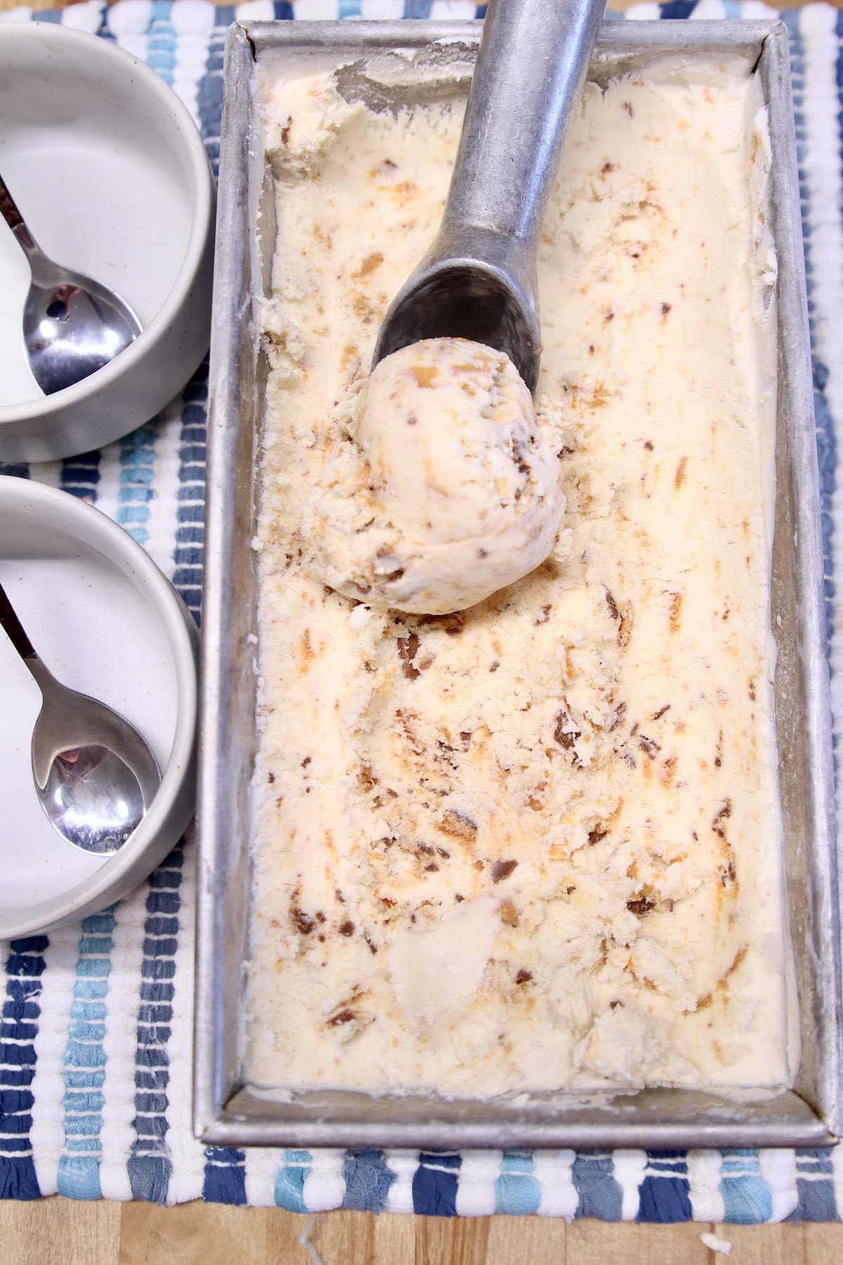 No churn ice cream in a loaf pan with a ice cream scoop, 2 bowls with spoons.
