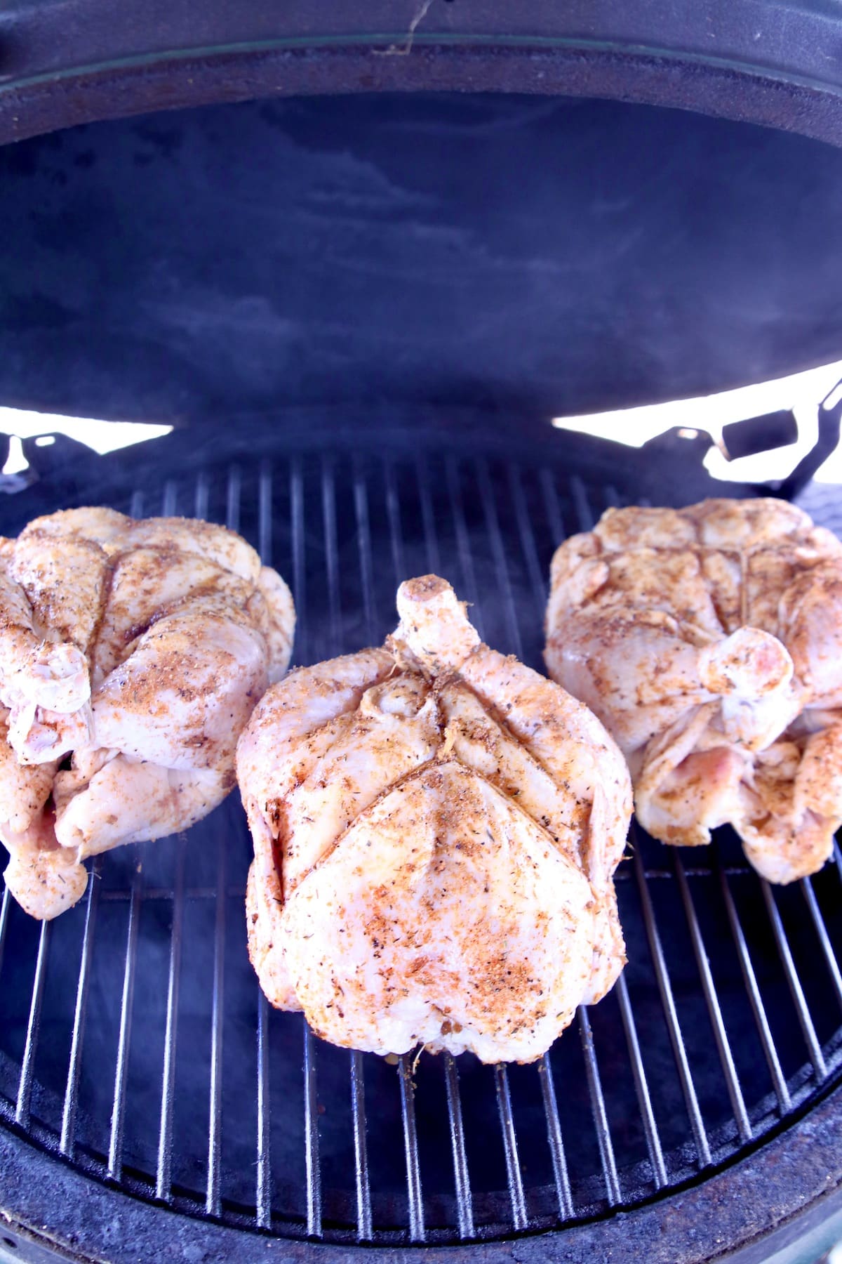 3 whole chickens with dry rub on a grill.