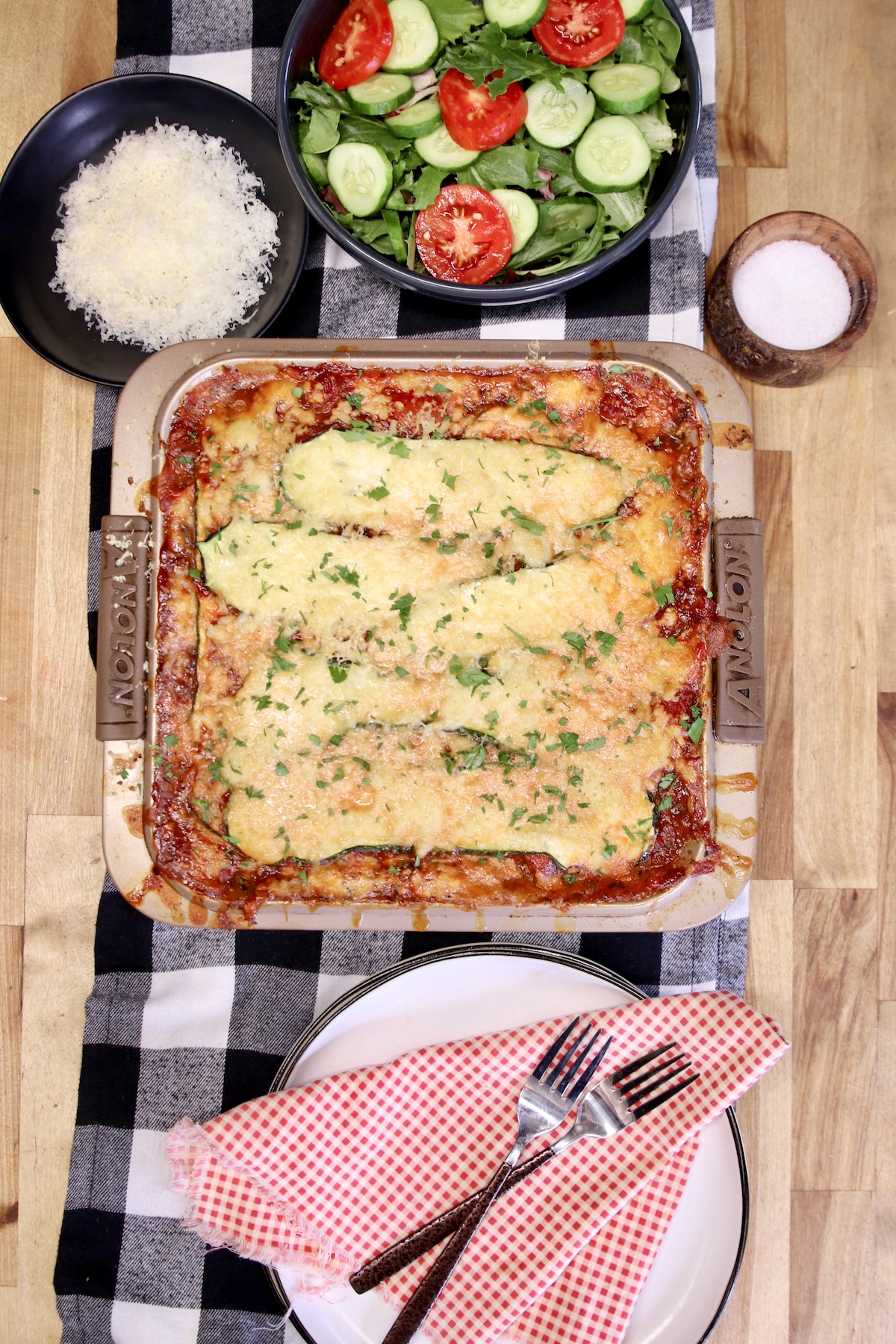 Overhead view of lasagna pan, salad, plates with forks.