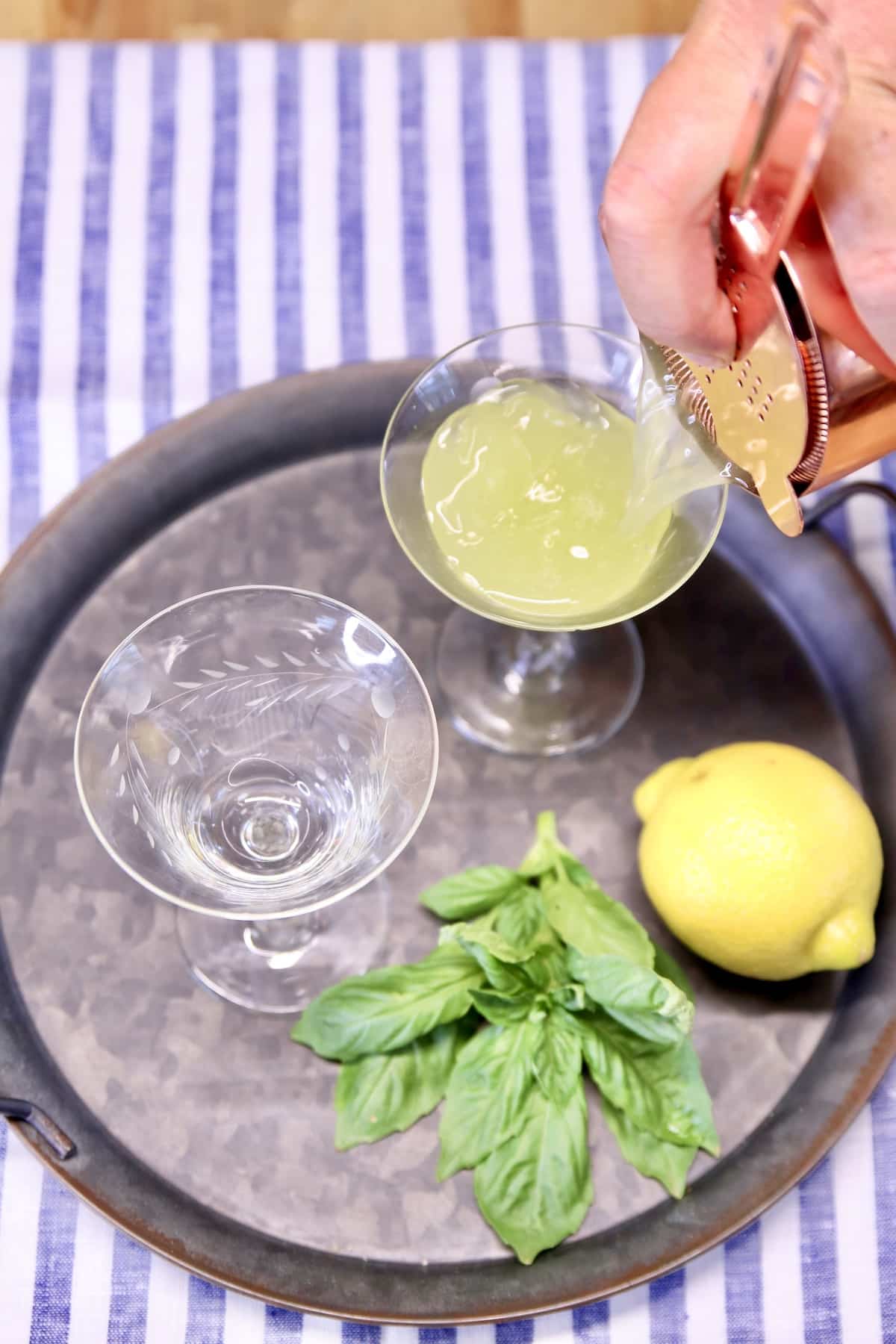 Pouring gin cocktail into 2 coupe glasses.