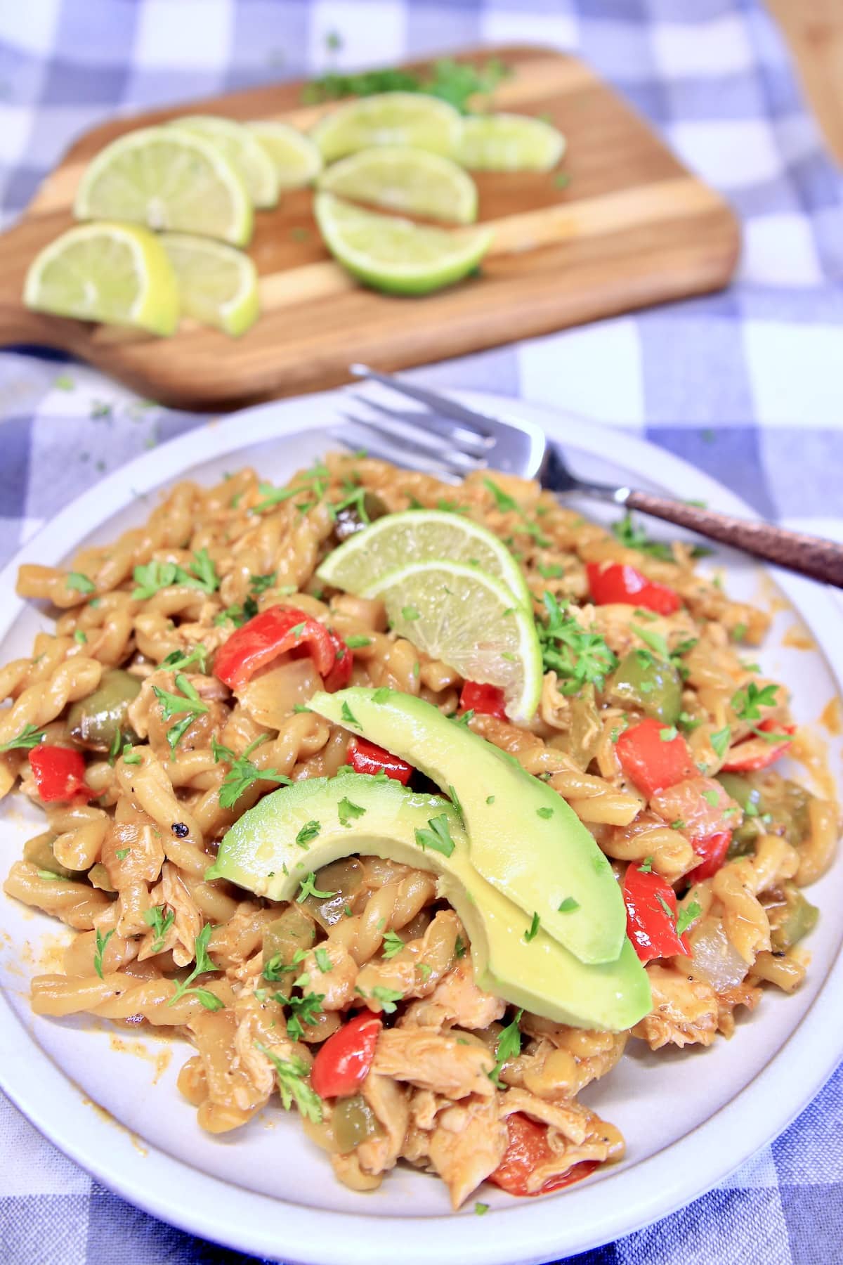 Plate of chicken and pasta with lime slices and avocado slices.