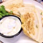 Chicken quesadilla cut into triangles, with sour cream and cilantro.