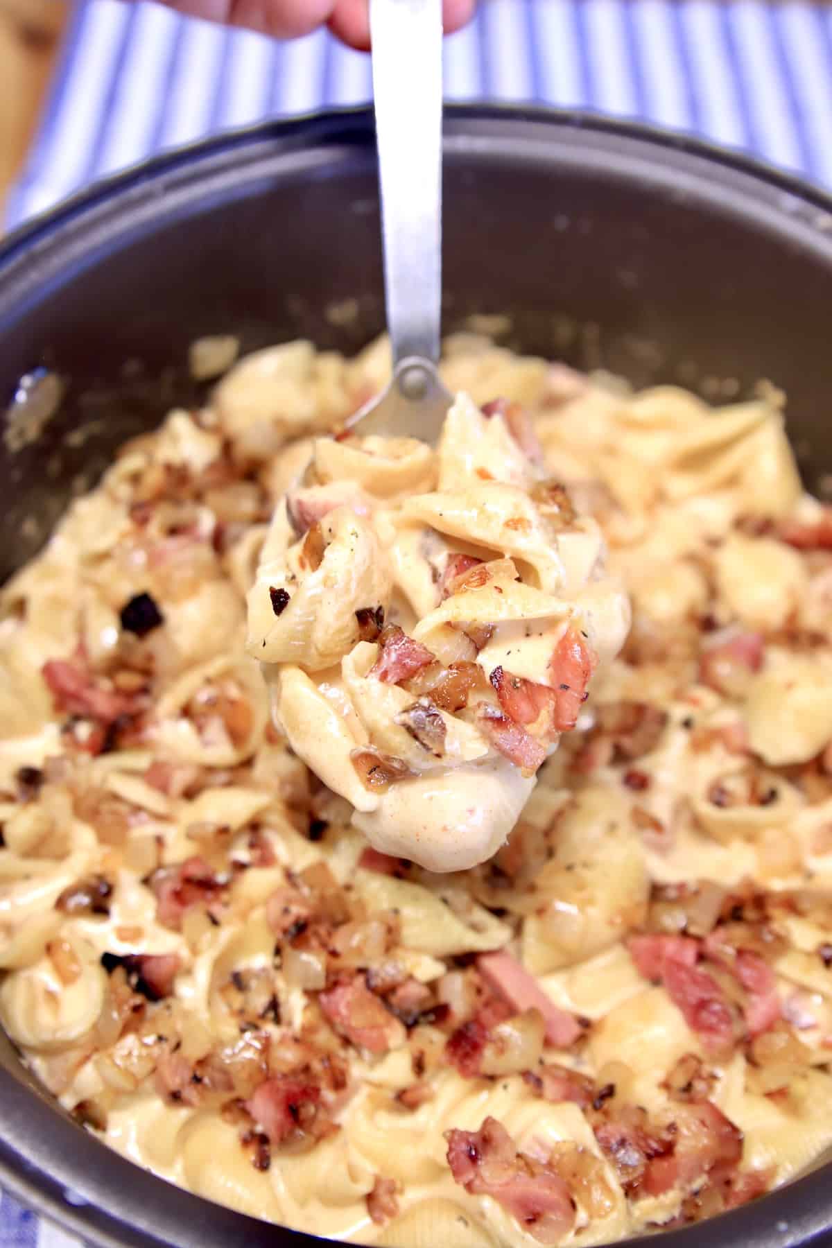 Spoonful of pasta with ham in a dutch oven.