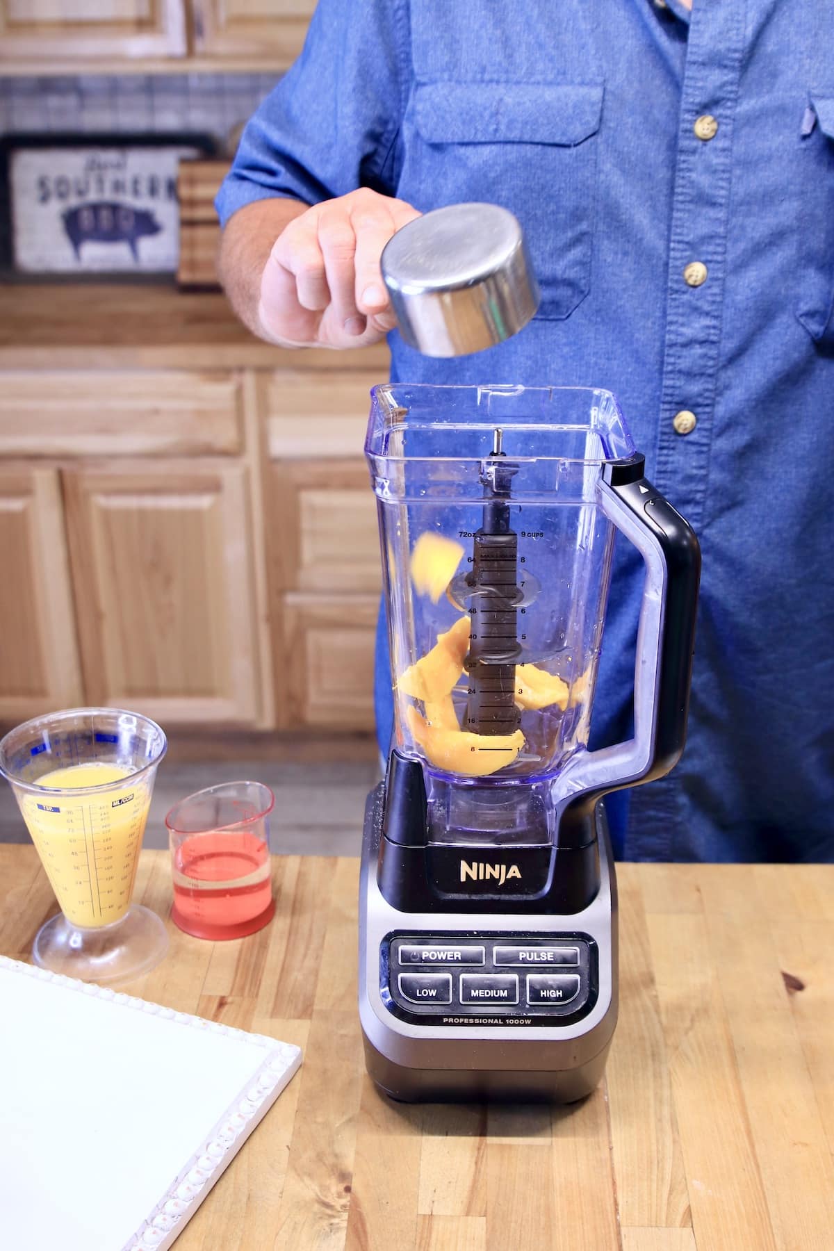 Man adding sliced mango to blender.